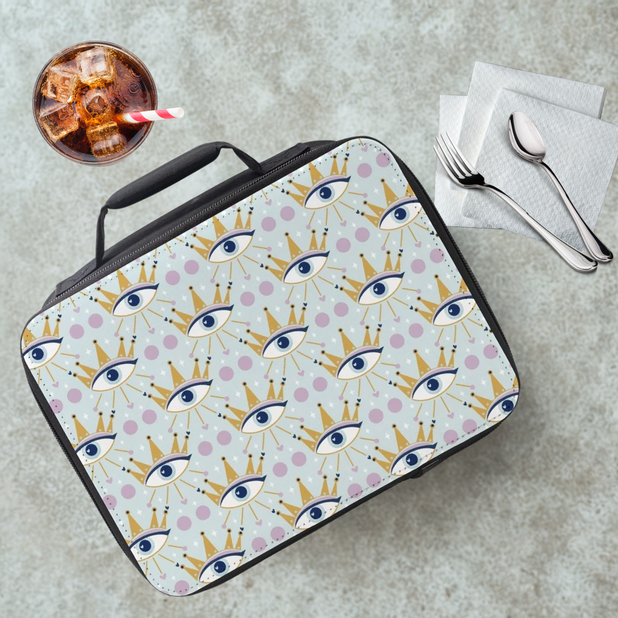 Lunch bag with a celestial eye pattern on a table with a drink and utensils.