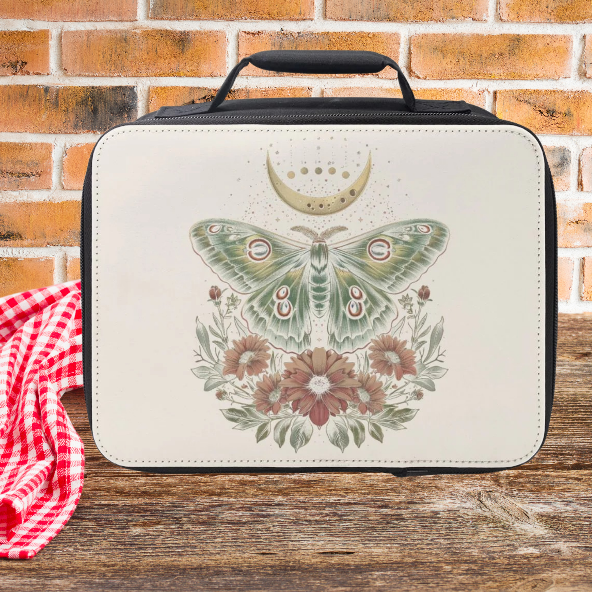 White lunch bag with celestial moth design on a wooden picnic table and brick wall background