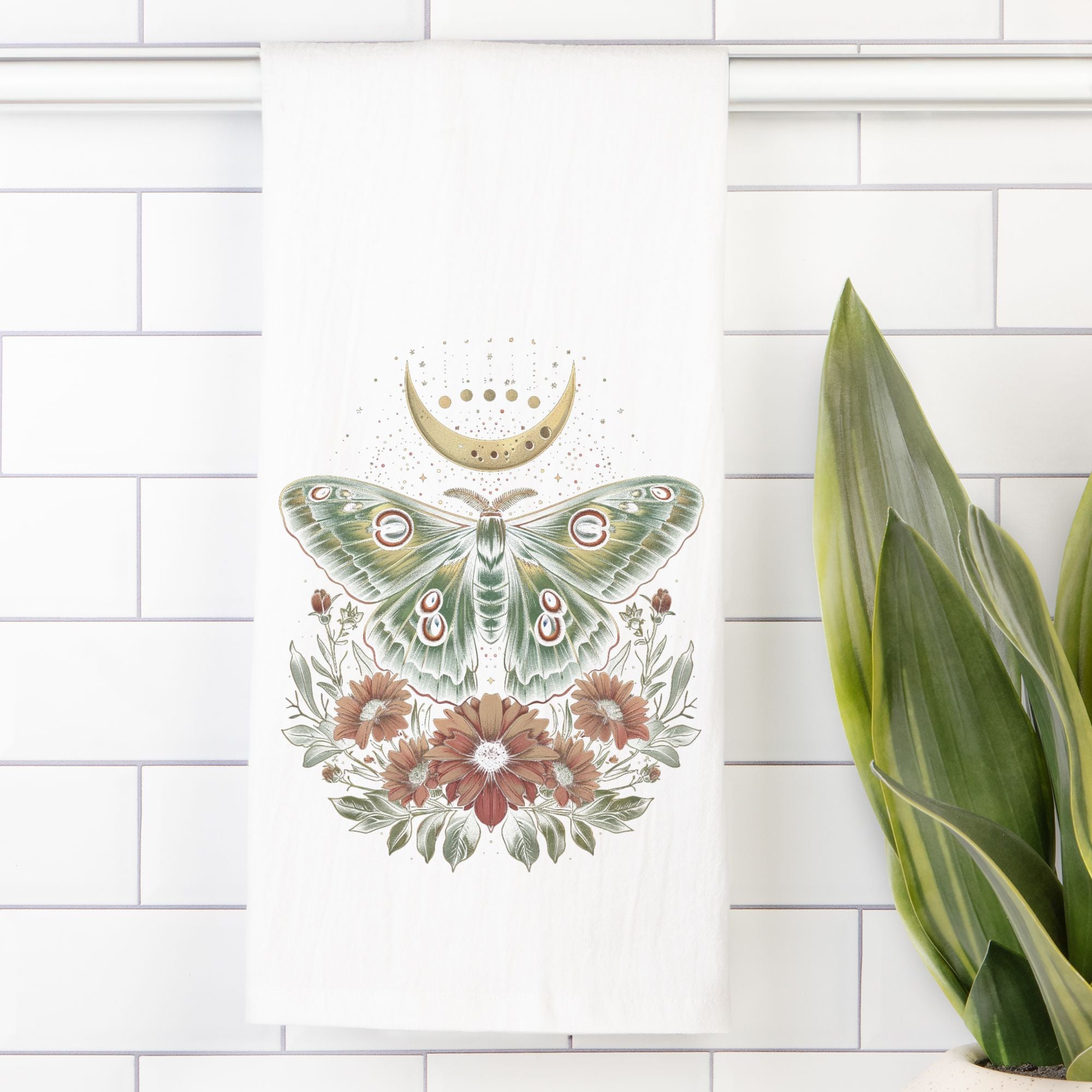 Decorative tea towel with a green moth and flowers design on a white tiled wall.