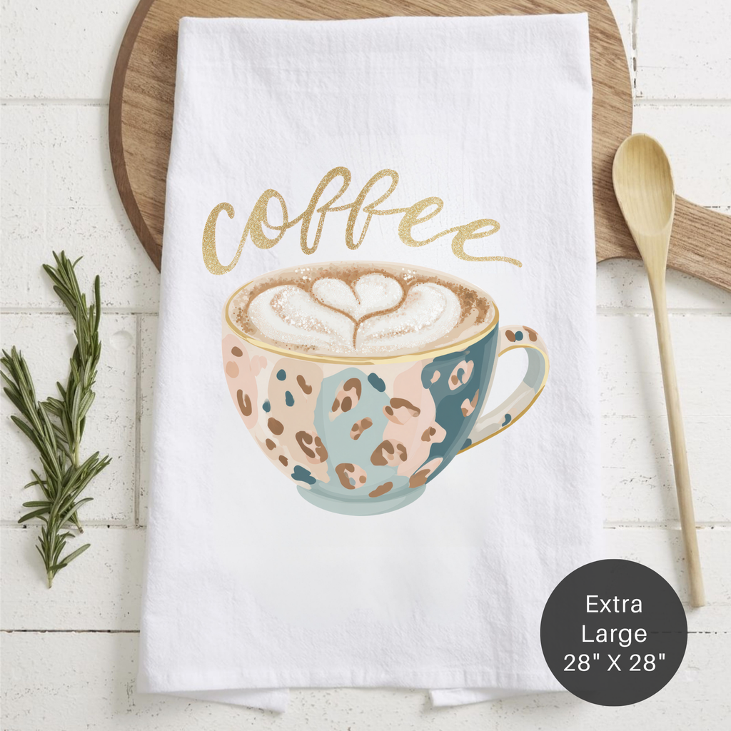 White towel with a coffee-themed design featuring a cup and the word 'coffee', placed on a wooden surface with a spoon and rosemary.