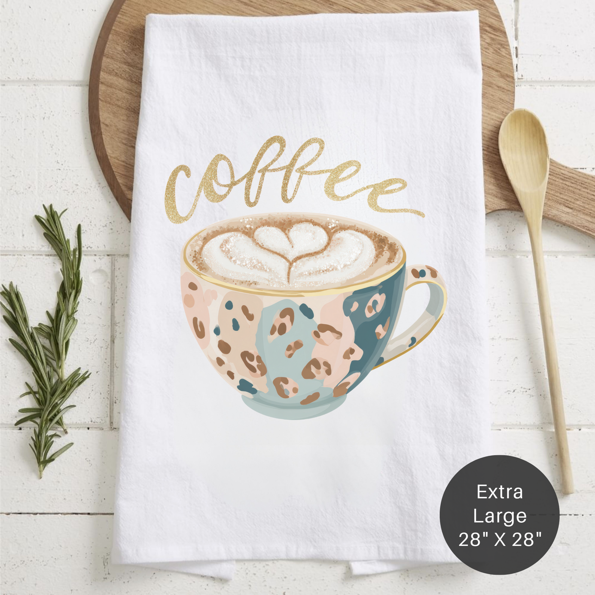 White towel with a coffee-themed design featuring a cup and the word 'coffee', placed on a wooden surface with a spoon and rosemary.