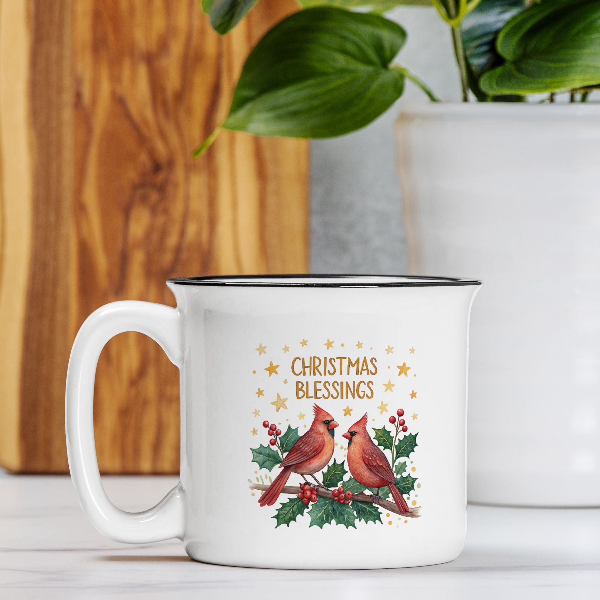 White mug with Christmas design featuring cardinals and holly, placed on a surface with a wooden board and plant in the background.