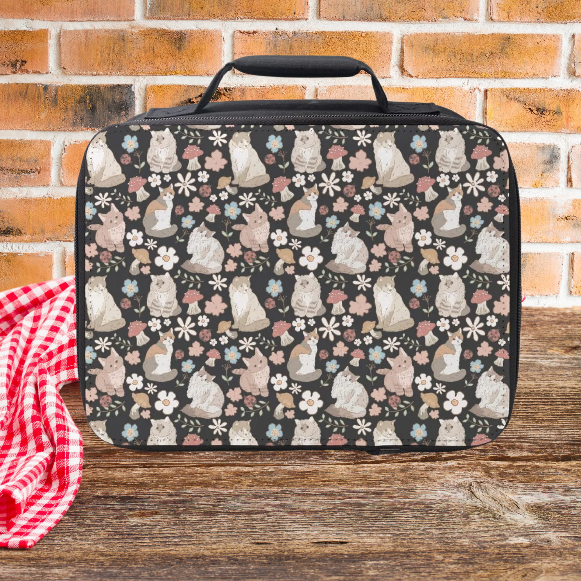 Lunch bag with cats and floral pattern on a wooden surface with a brick wall background