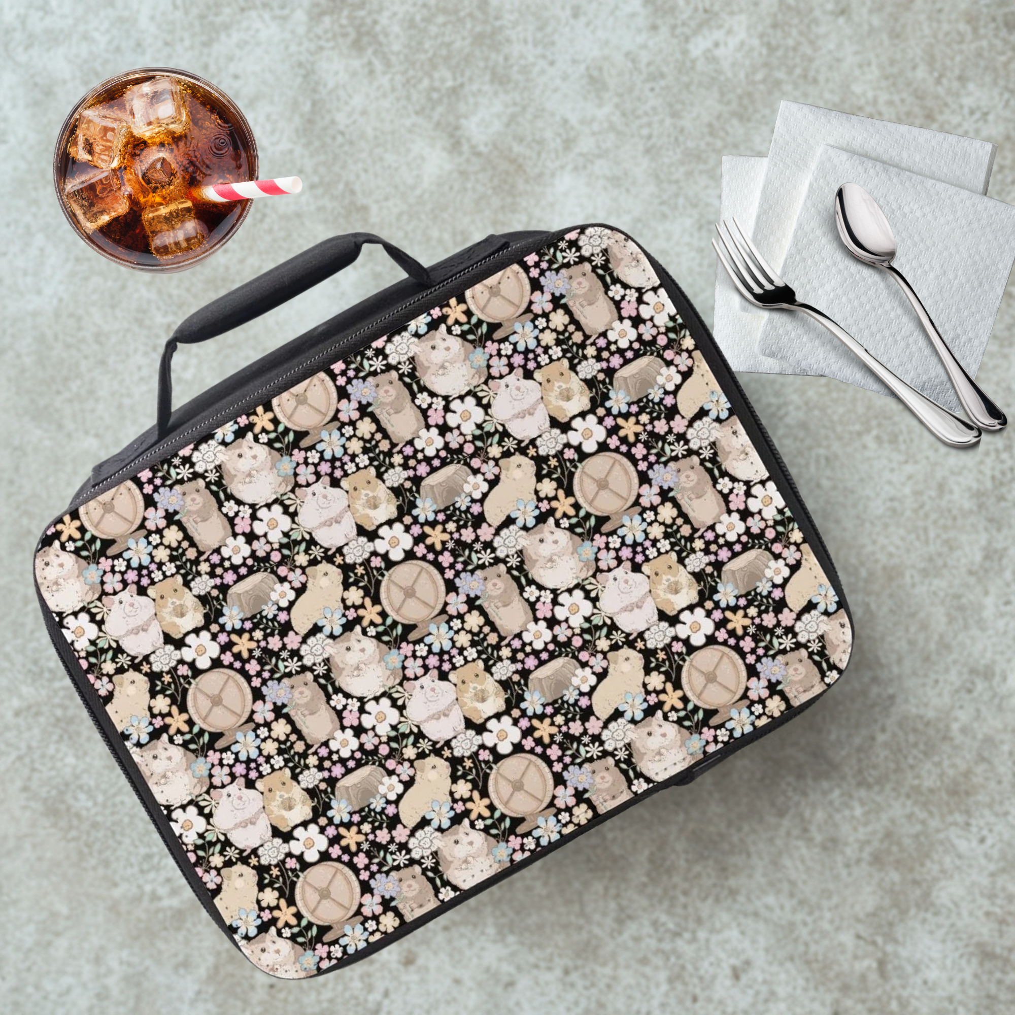Lunch bag with hamster and flower pattern on a cafeteria table with a drink and utensils.