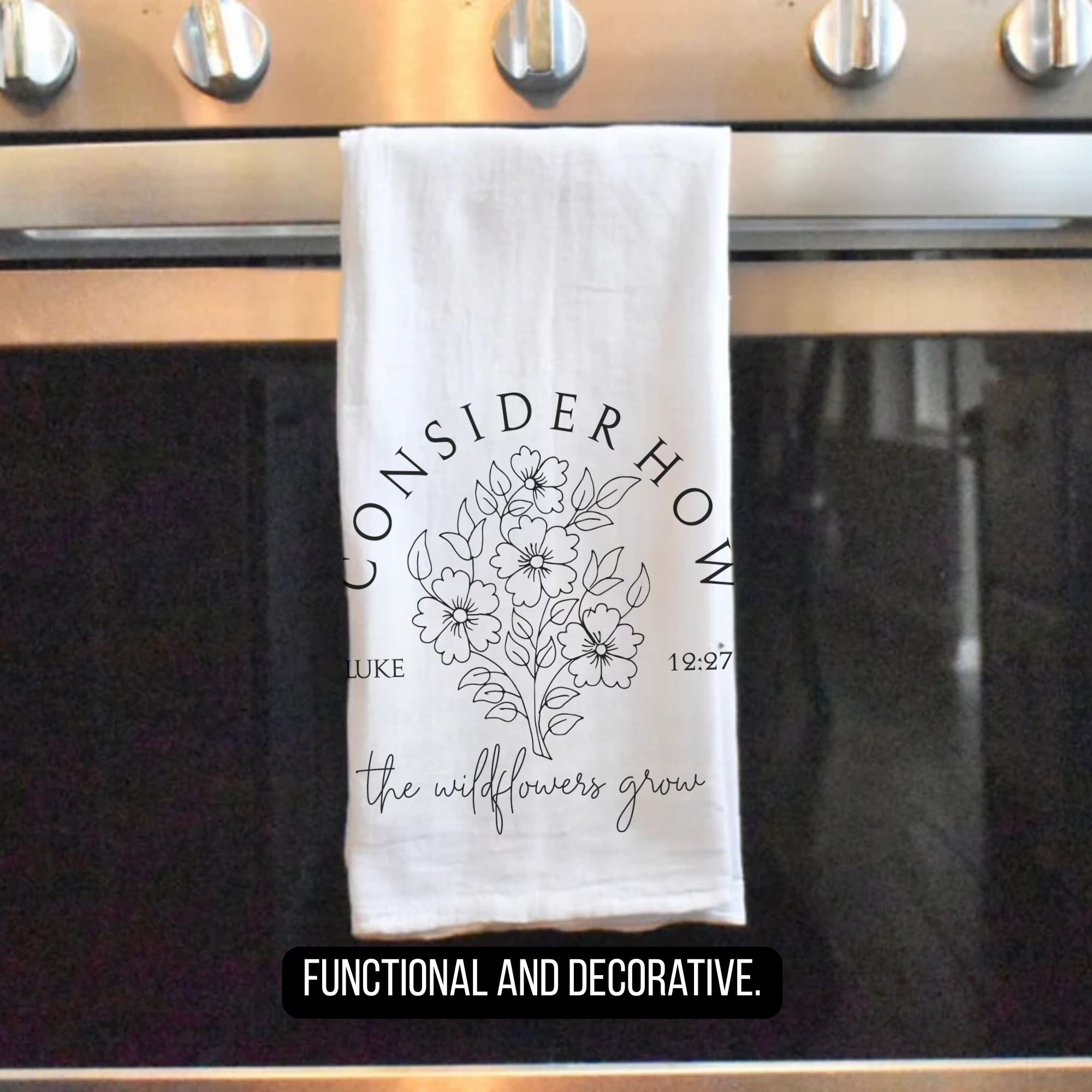 Decorative tea towel with floral design and text hanging on a stove.