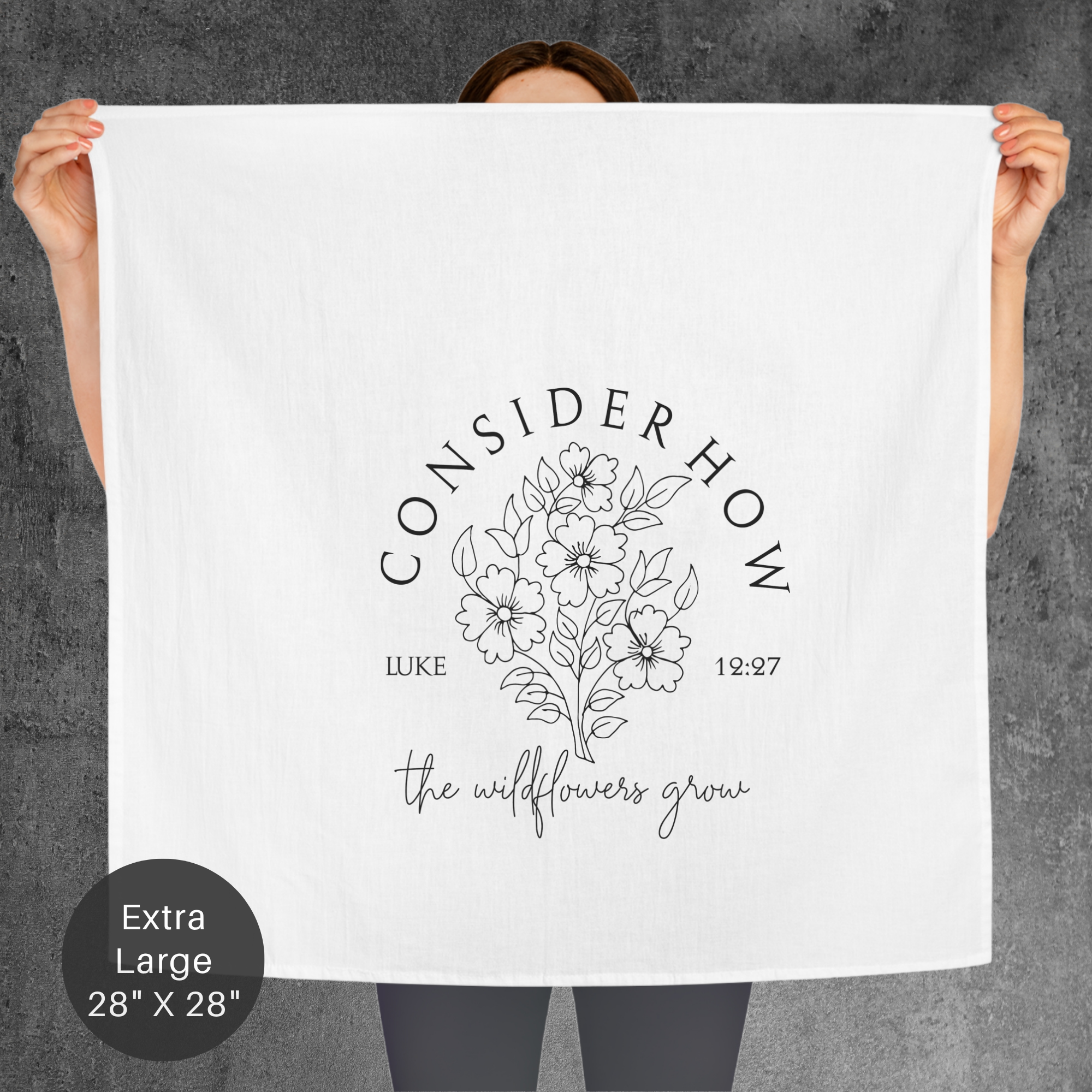 Person holding an extra large white towel with floral design and text 'Consider How The Wildflowers Grow' on a gray background