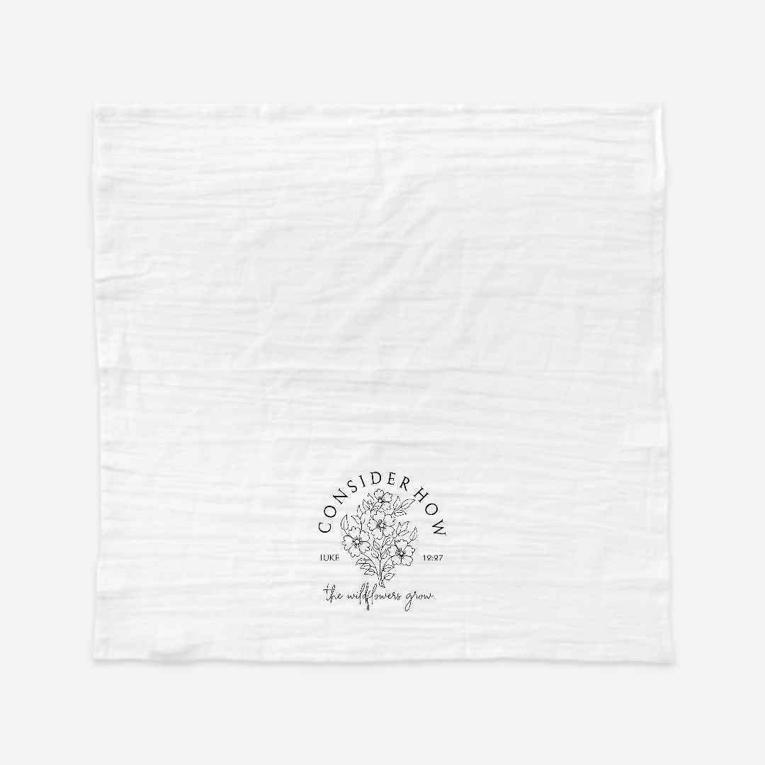 White tea towel with black floral logo design and text 'Consider How The Wildflowers Grow' on a white background