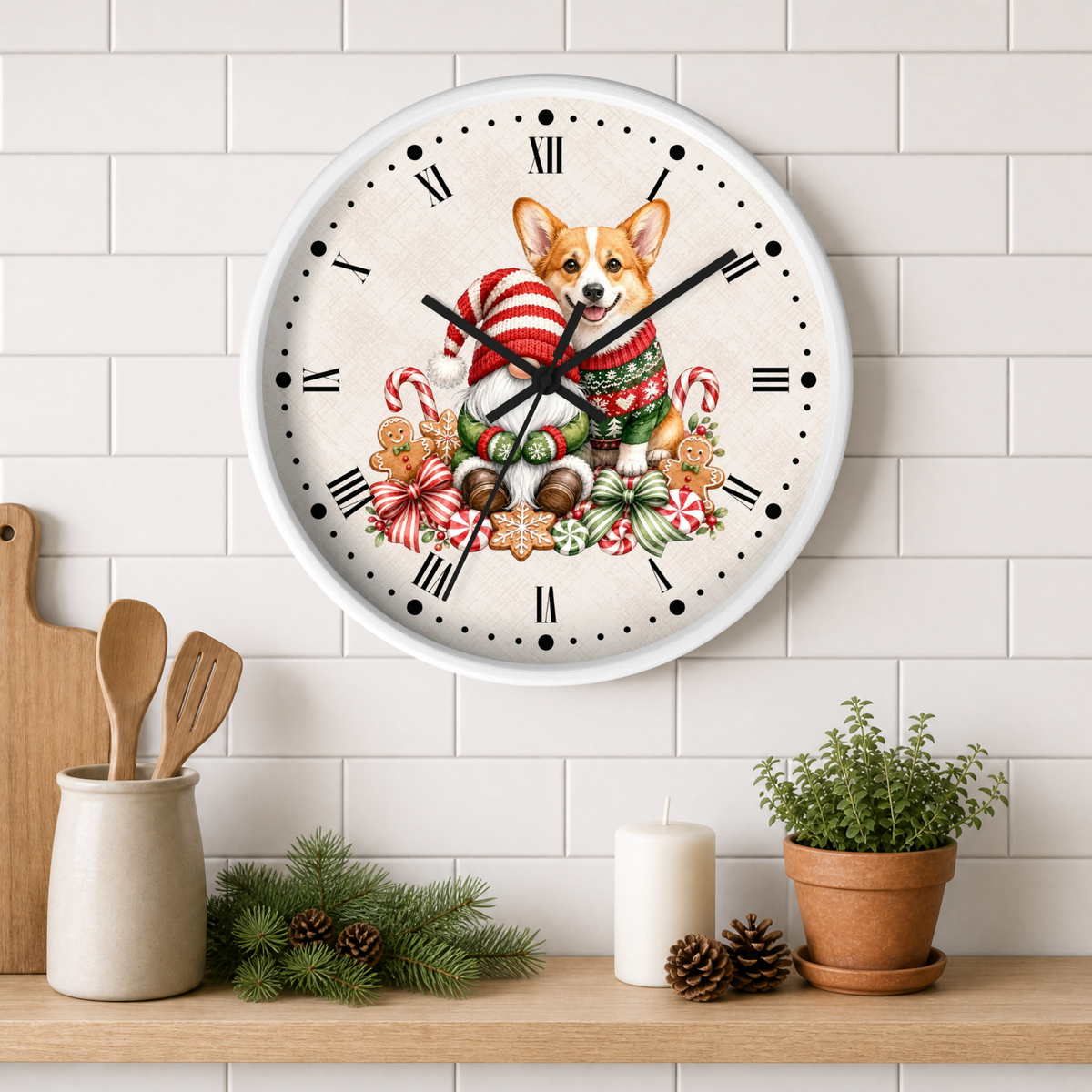 A round wall clock with a white face and black Roman numerals, featuring a festive illustration of a corgi dog in a red-and-white striped sweater surrounded by candy canes, ornaments, and gingerbread cookies. The clock is mounted on a white subway-tile wall above a wooden shelf styled with kitchen utensils, pine branches, a candle, and a potted plant.