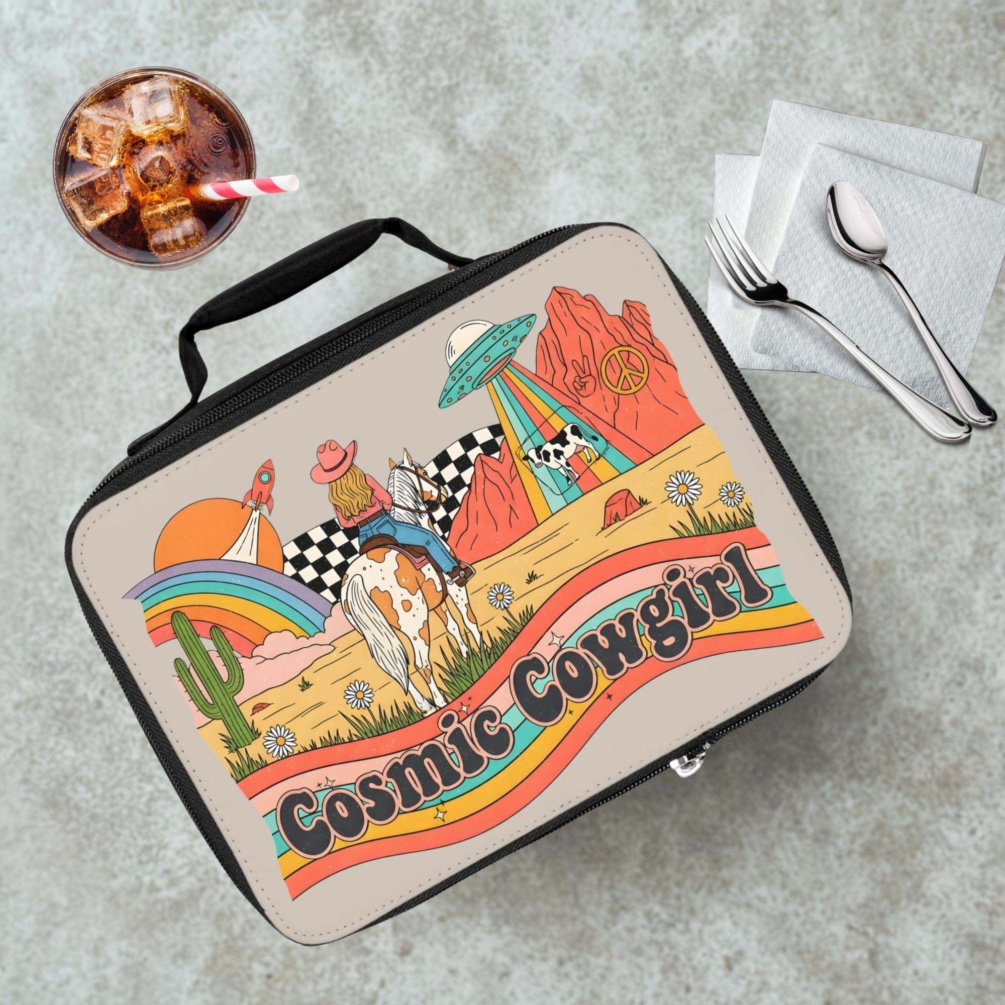 Lunch box with 'Cosmic Cowgirl' design on a cafeteria table with a drink and utensils.