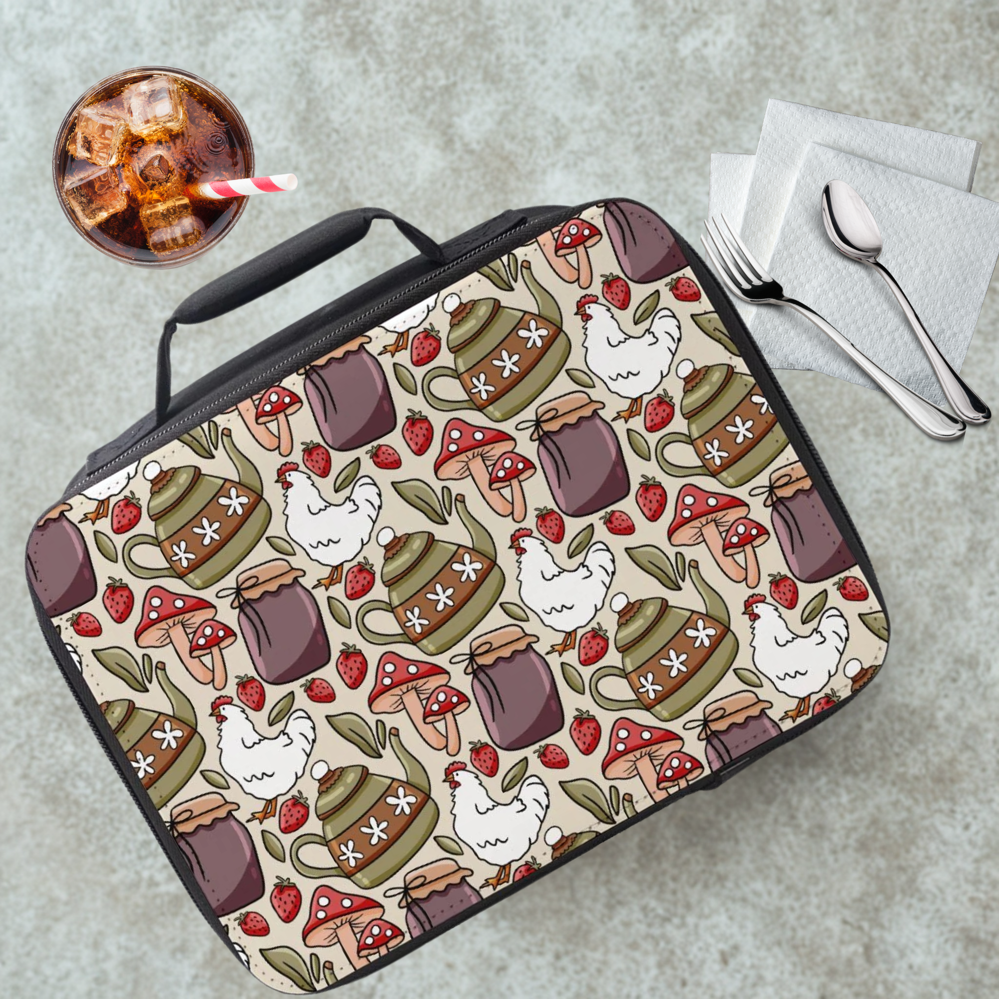 Lunch bag with a pattern of teapots, chickens, and strawberries on a cafeteria table with a drink and utensils.