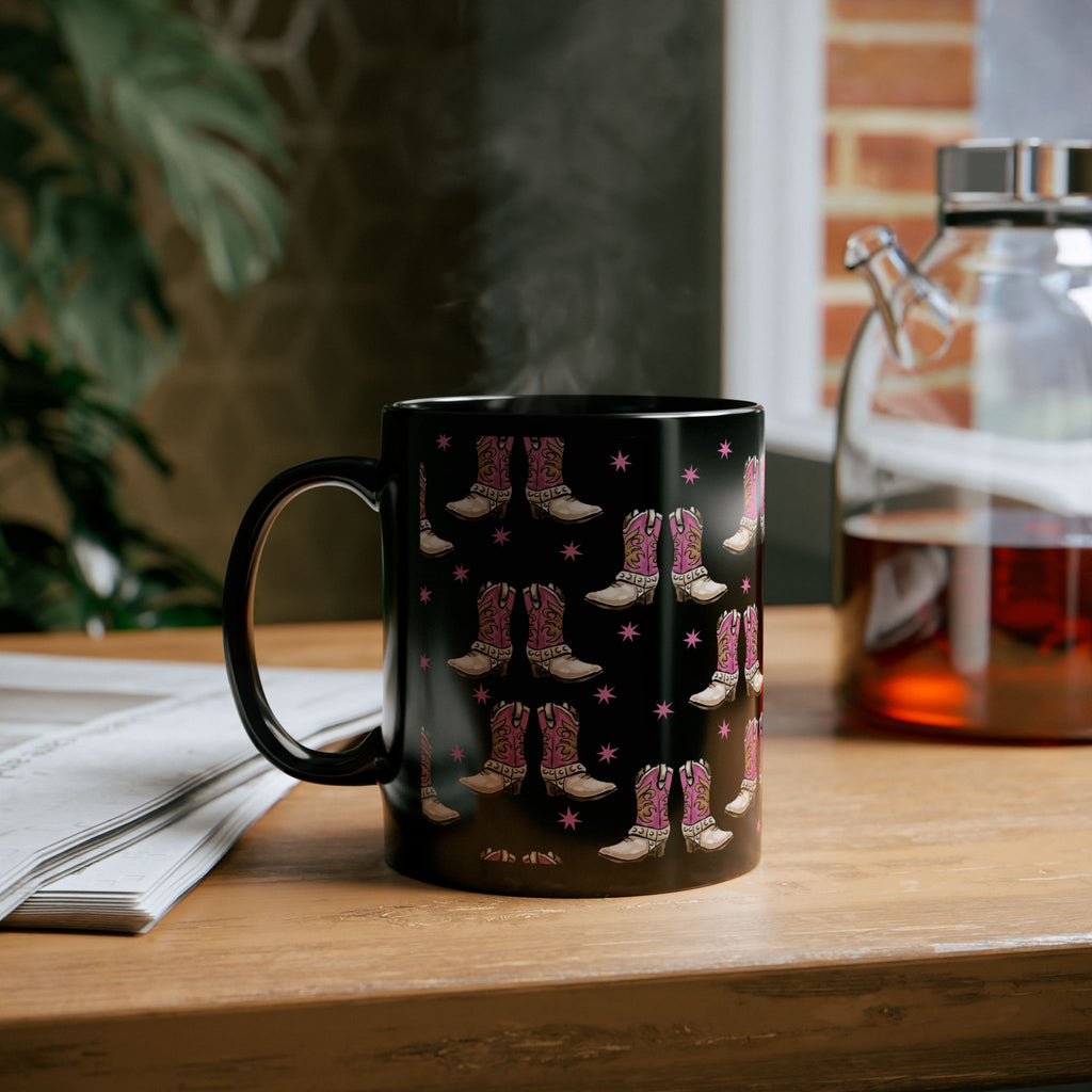 Black mug with pink cowboy boot design on a wooden surface