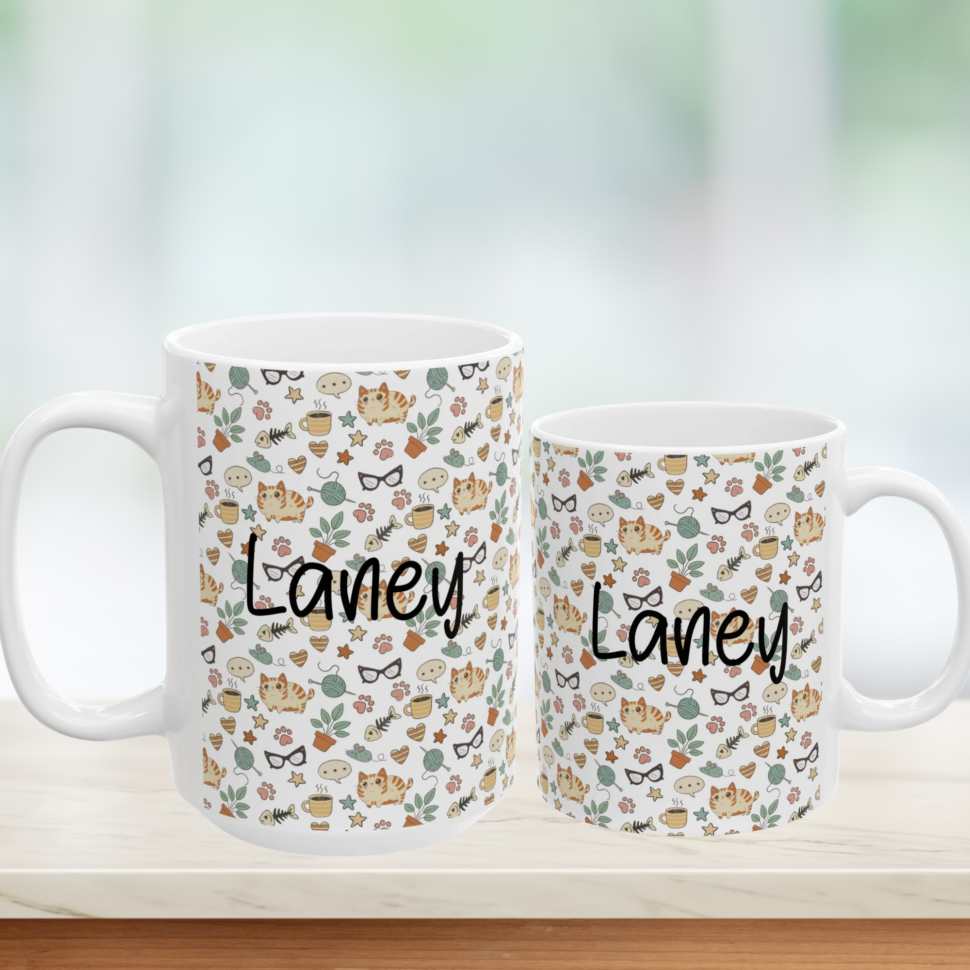 Two mugs with 'Laney' branding and a pattern of cats, flowers, and glasses on a blurred background.