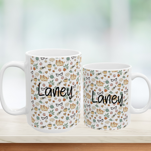 Two mugs with 'Laney' branding and a pattern of cats, flowers, and glasses on a blurred background.
