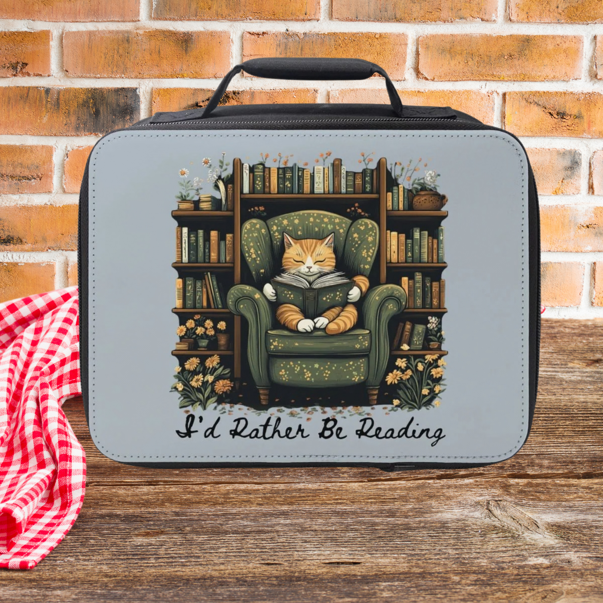 Lunch bag with a cat reading a book design on a wooden surface with a brick wall background.