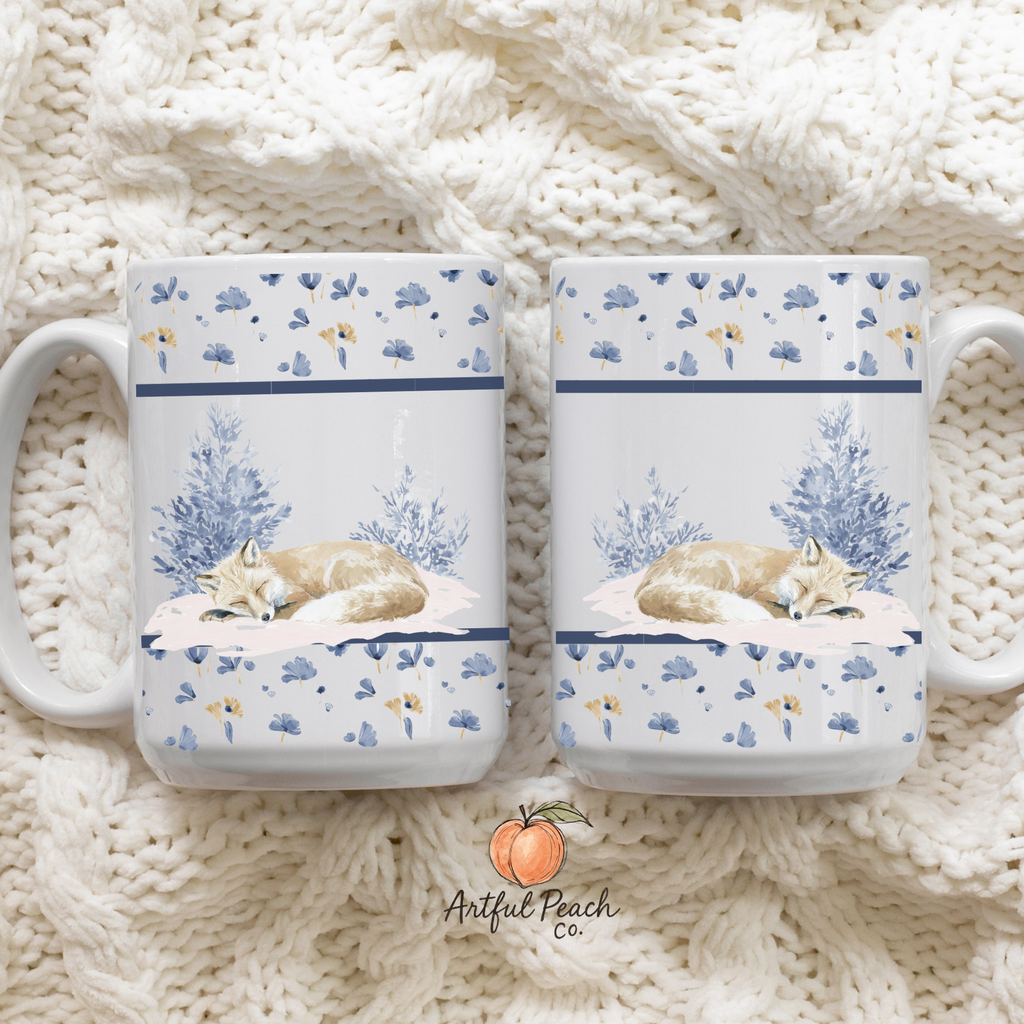 Two mugs with a design of a fox sleeping on a cloud, placed on a knitted surface. The brand 'Artful Peach' is visible.