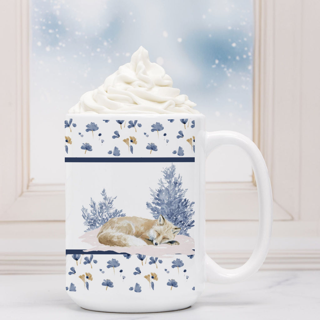 White mug with winter-themed design featuring a fox and trees, filled with hot chocolate and whipped cream.