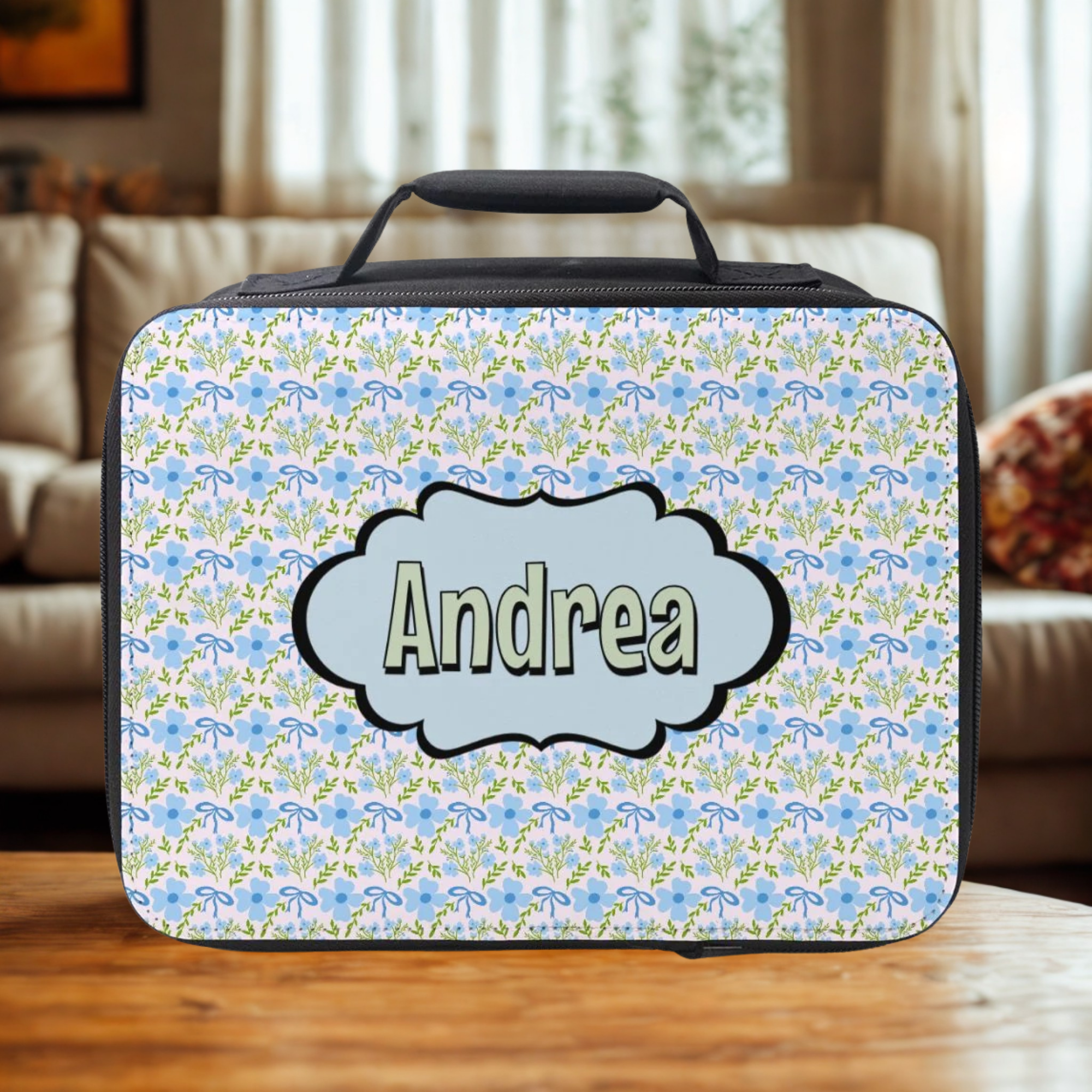 Floral patterned lunch bag with 'Andrea' on a wooden living room table.