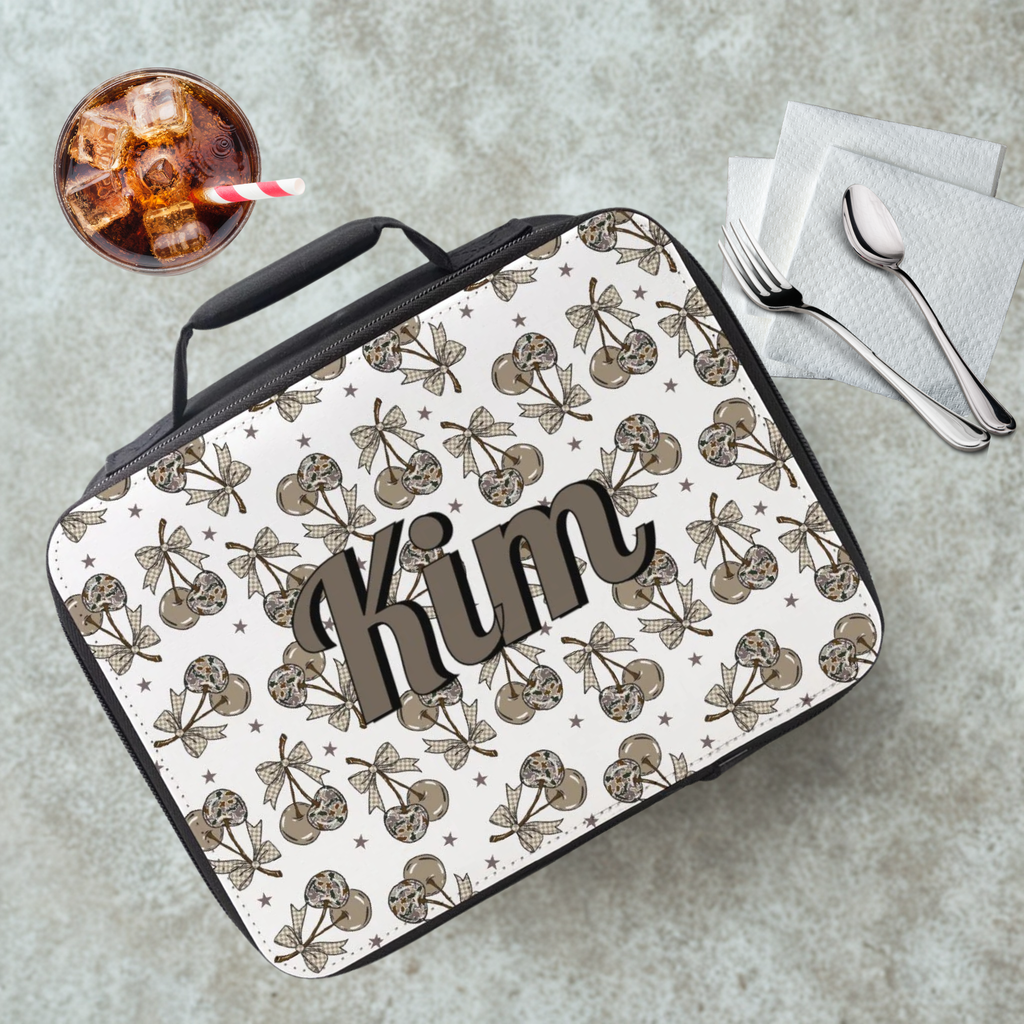 Lunch bag with a camouflage cherry pattern and personalized name on a cafeteria table with a drink and utensils.