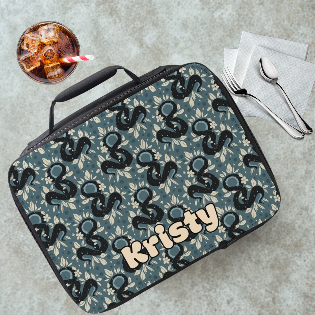  insulated lunch bag with snake pattern and 'Kristy' name, next to a drink and utensils on a cafeteria table.