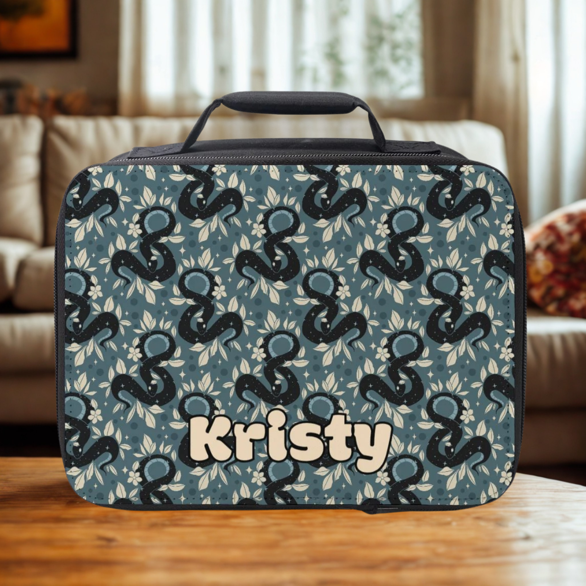 Celestial snake patterned lunch bag with 'Kristy' custom text on a wooden coffee table in a cozy living room.