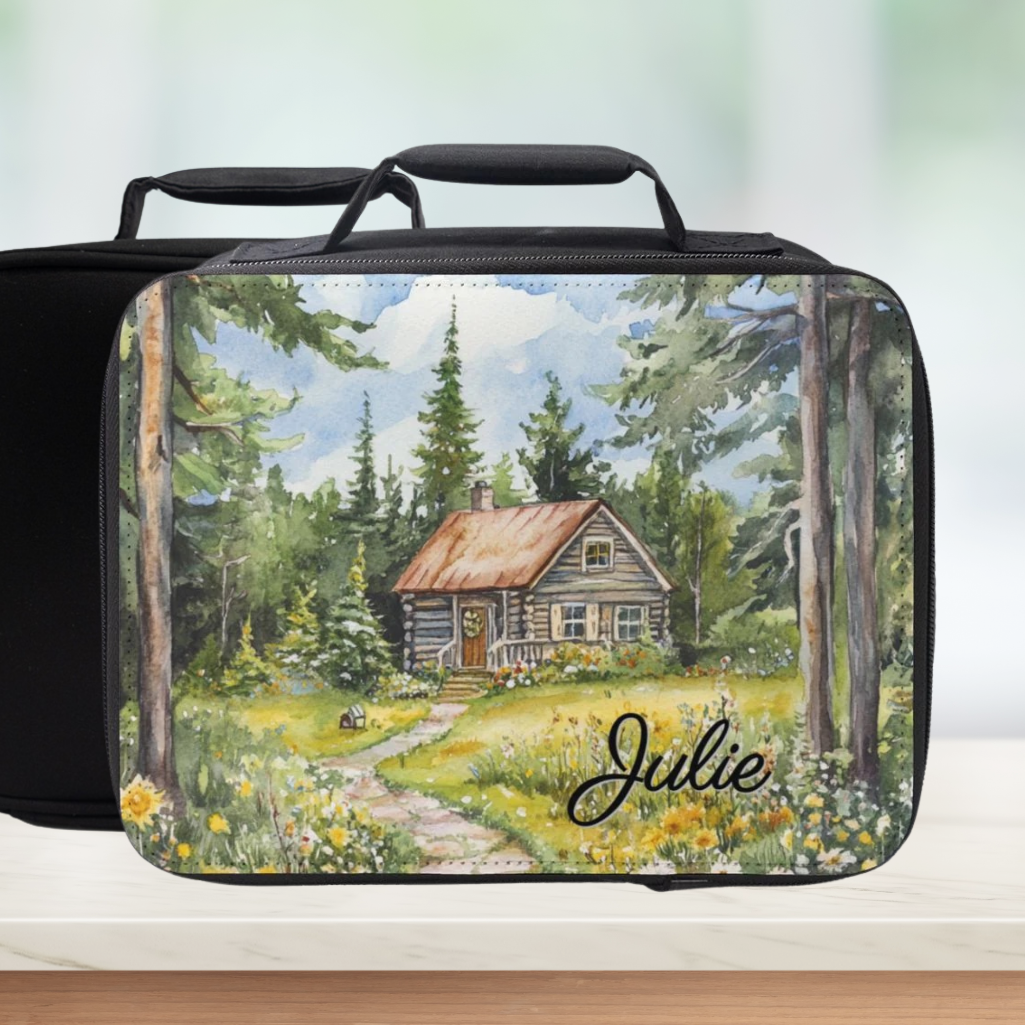 Black lunch bag with a painted design of a cabin in the woods and the name 'Julie' on a white background.