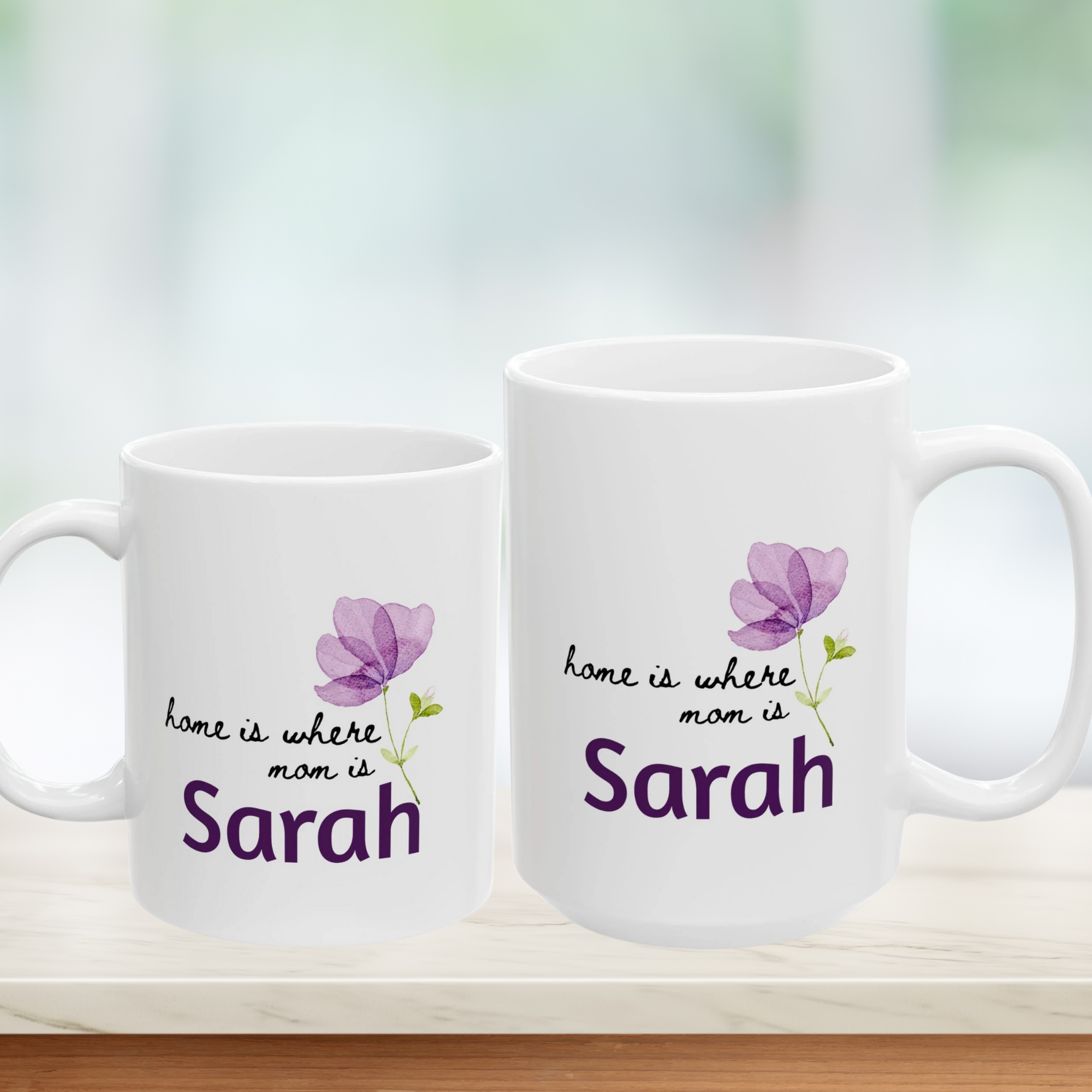 Two white mugs with purple floral designs and text on a blurred background