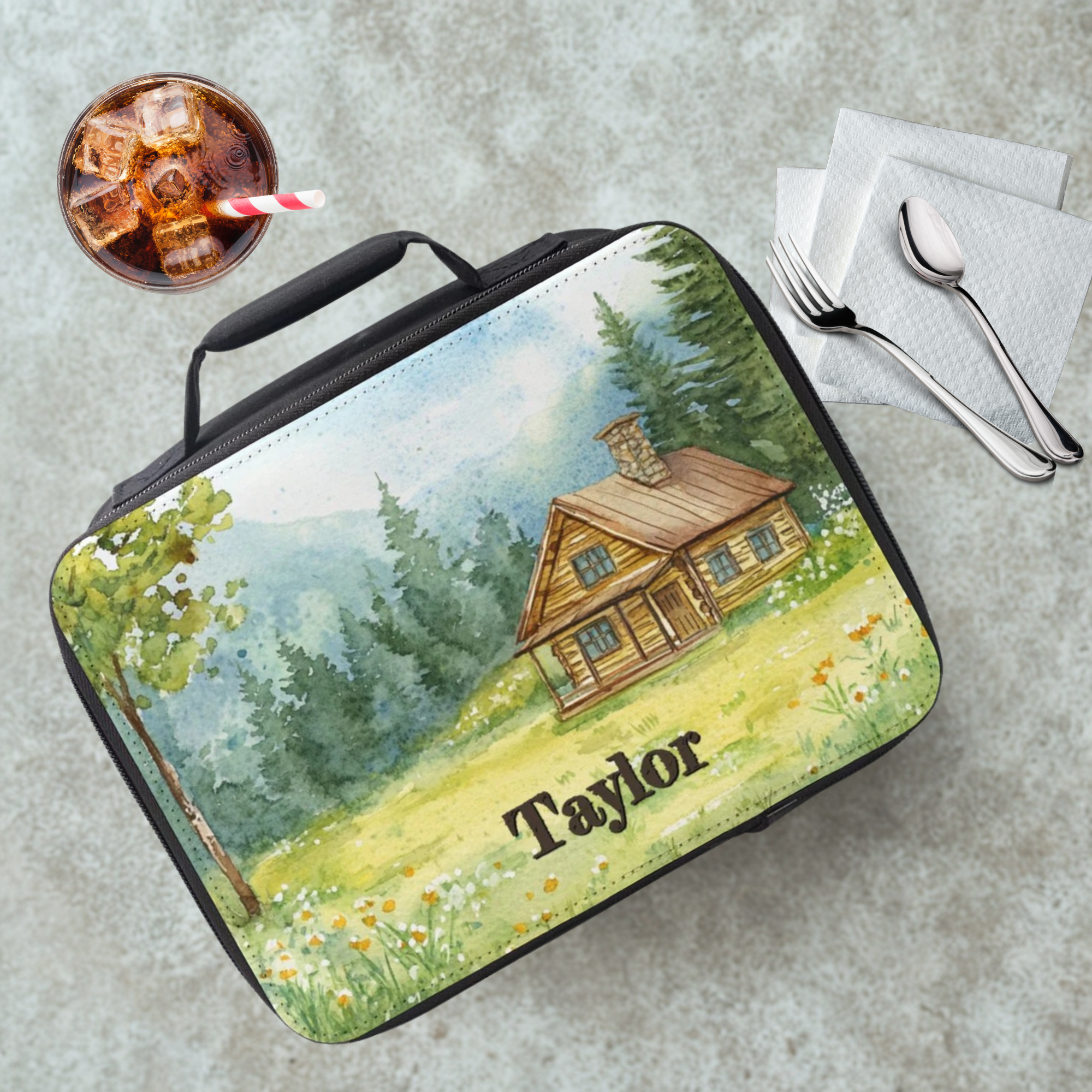 Lunch bag with a cabin design and personalized name on a cafeteria table with a drink and utensils.