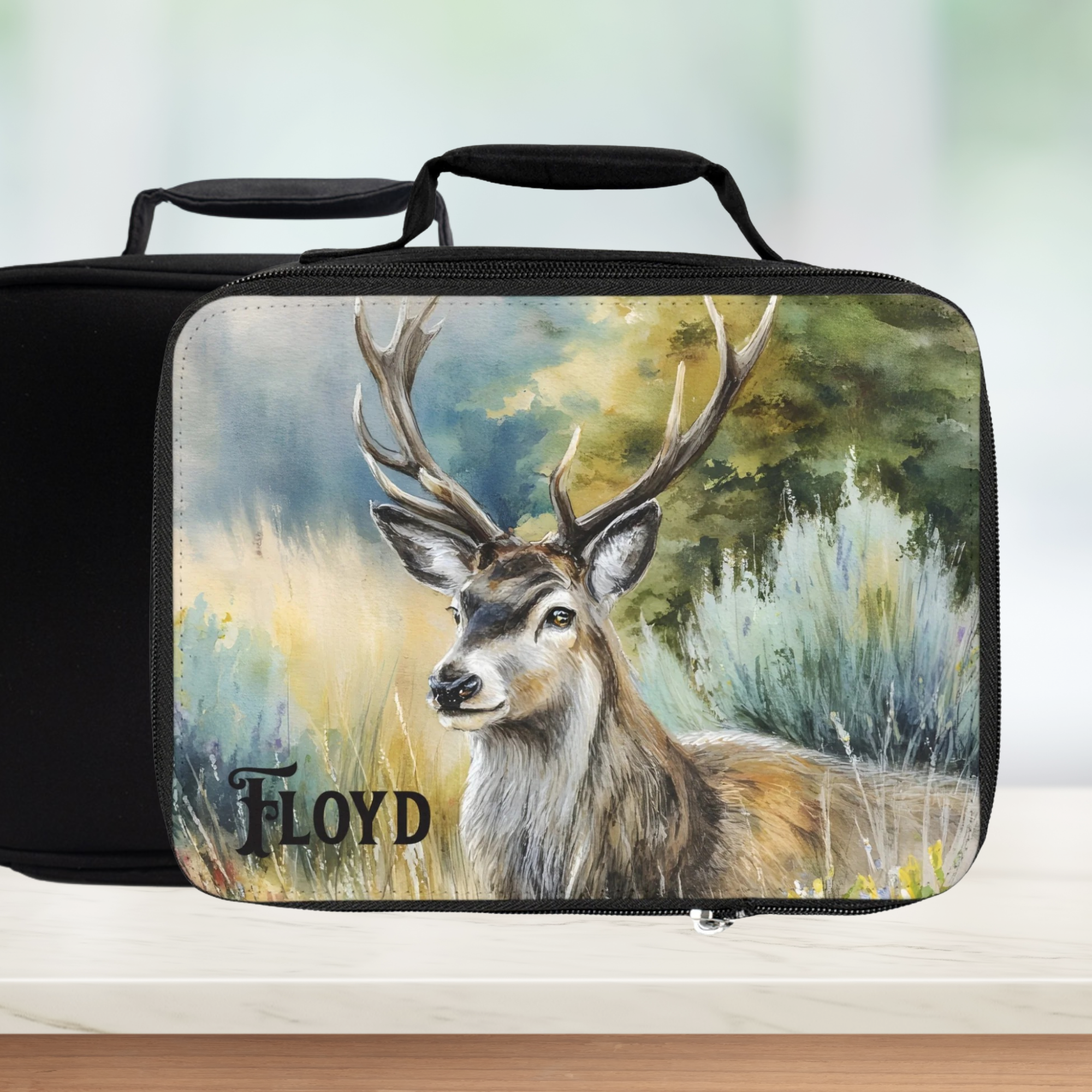 Black rectangular lunch bag with a deer painting design and 'Floyd' personalized text on a blurred nature background