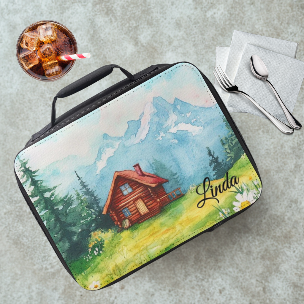  insulated lunch bag with a cabin design and the name 'Linda' on a cafeteria table with a drink and utensils.