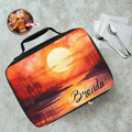 Lunch bag with sunset design and 'Brenda' text on a cafeteria table with a drink and utensils.
