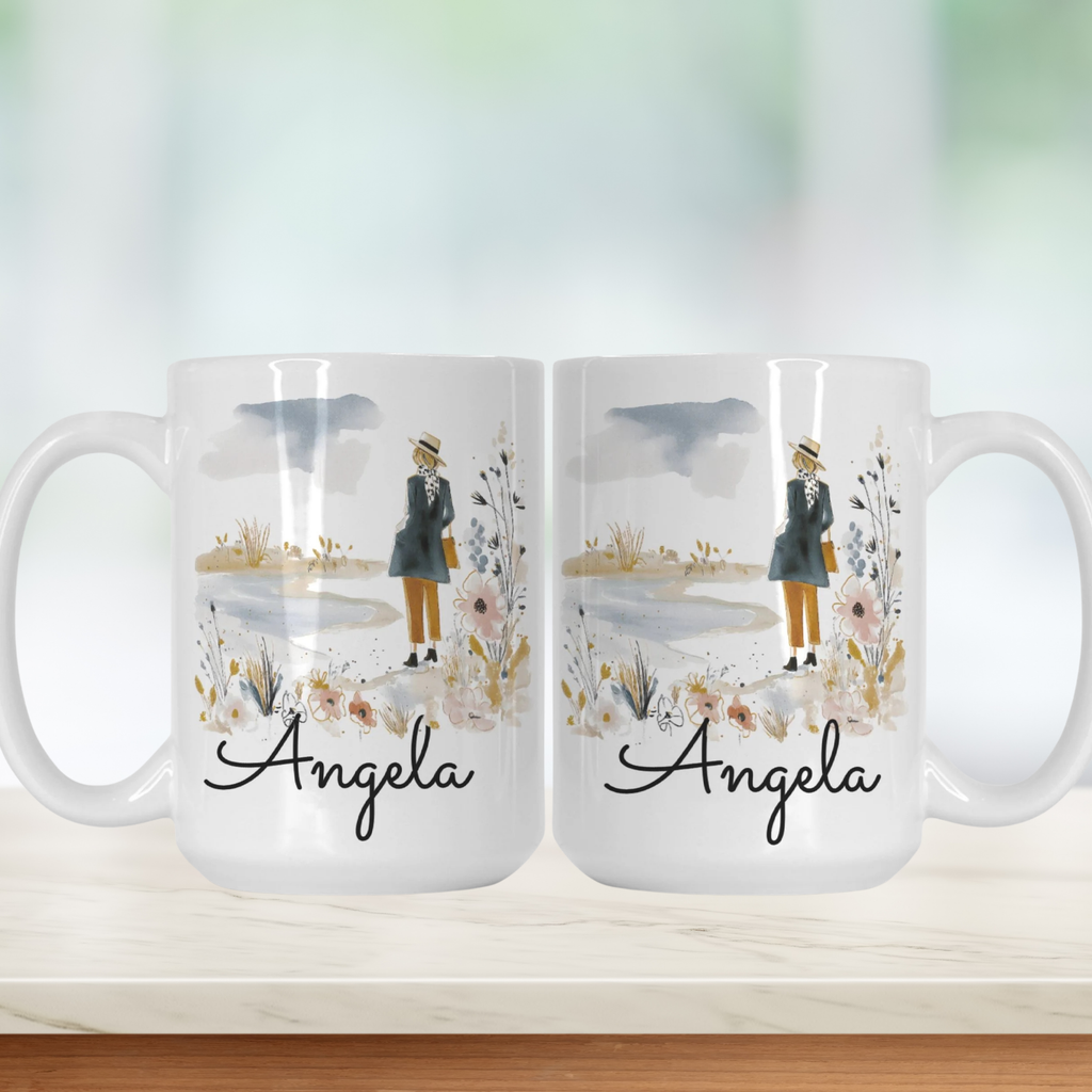 Two white mugs with a design of a person holding an umbrella, flowers, and the name 'Angela' on a light background.