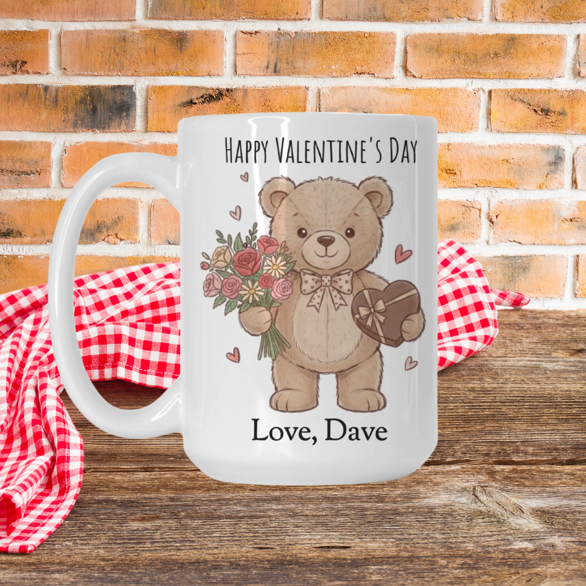 Valentine's Day mug with a bear design, flowers, and a heart, placed on a wooden picnic table with a red checkered cloth and brick wall background.