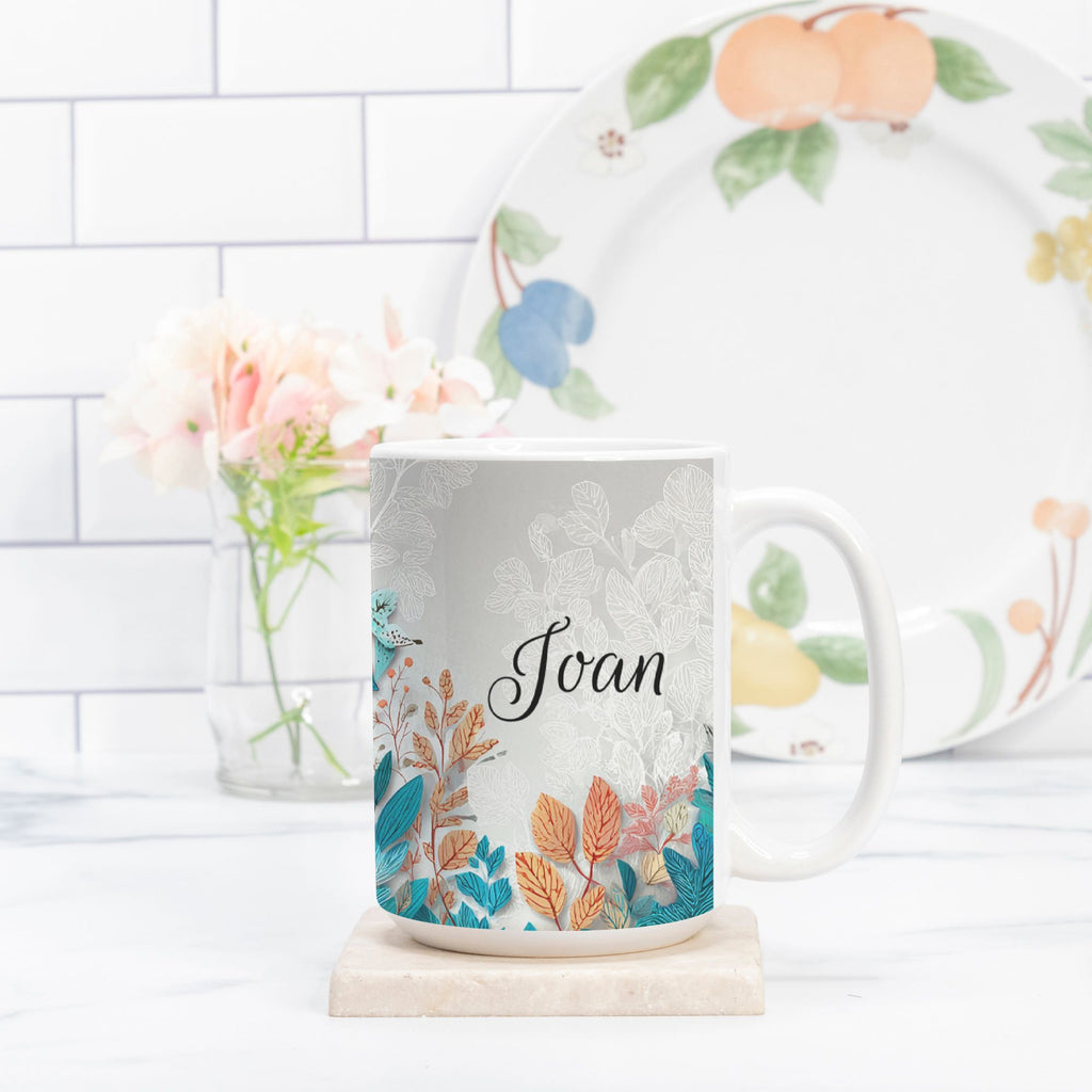Mug with floral design and 'Joan' text, placed on a marble coaster with a blurred background.