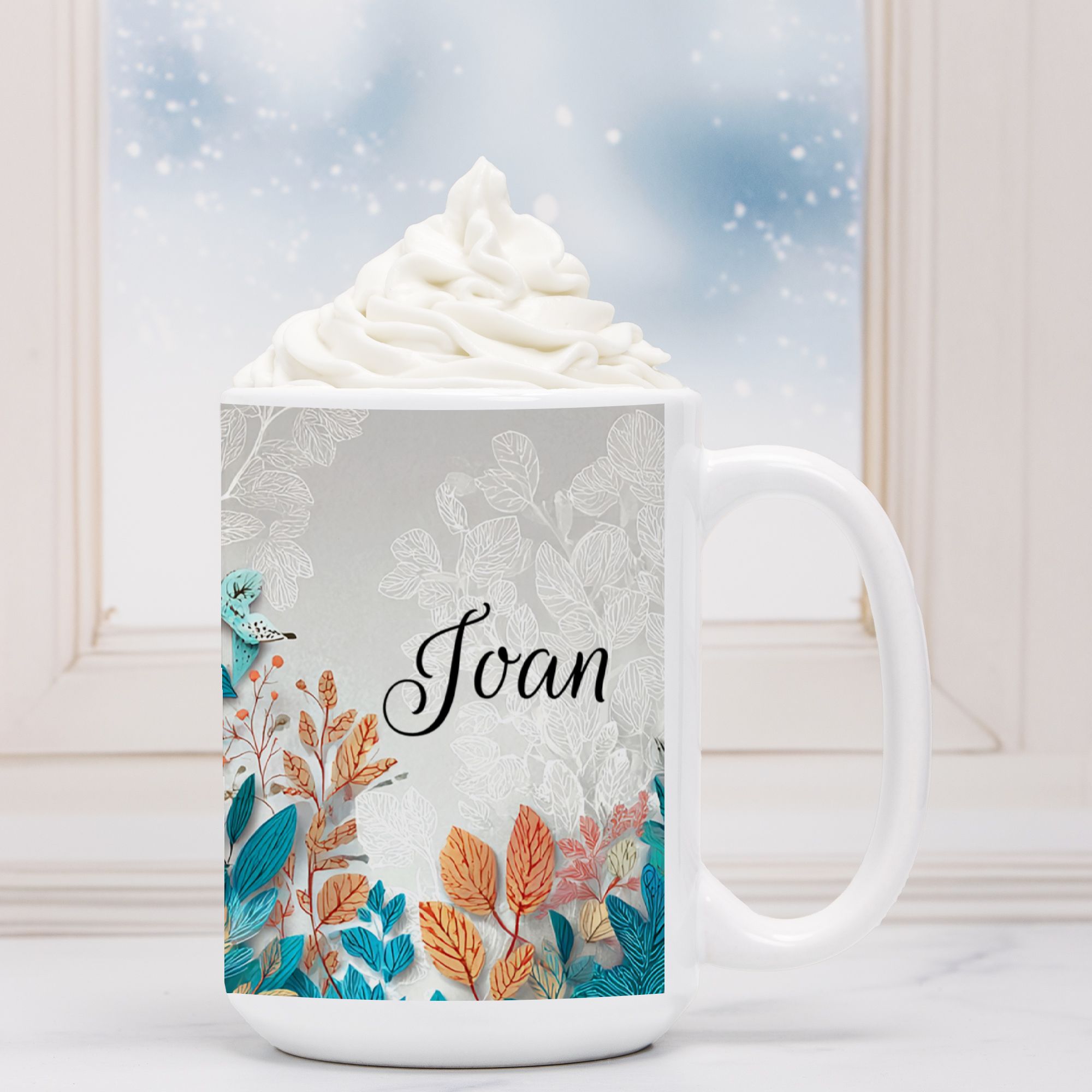 Mug with floral design and name 'Joan' filled with hot chocolate and whipped cream.