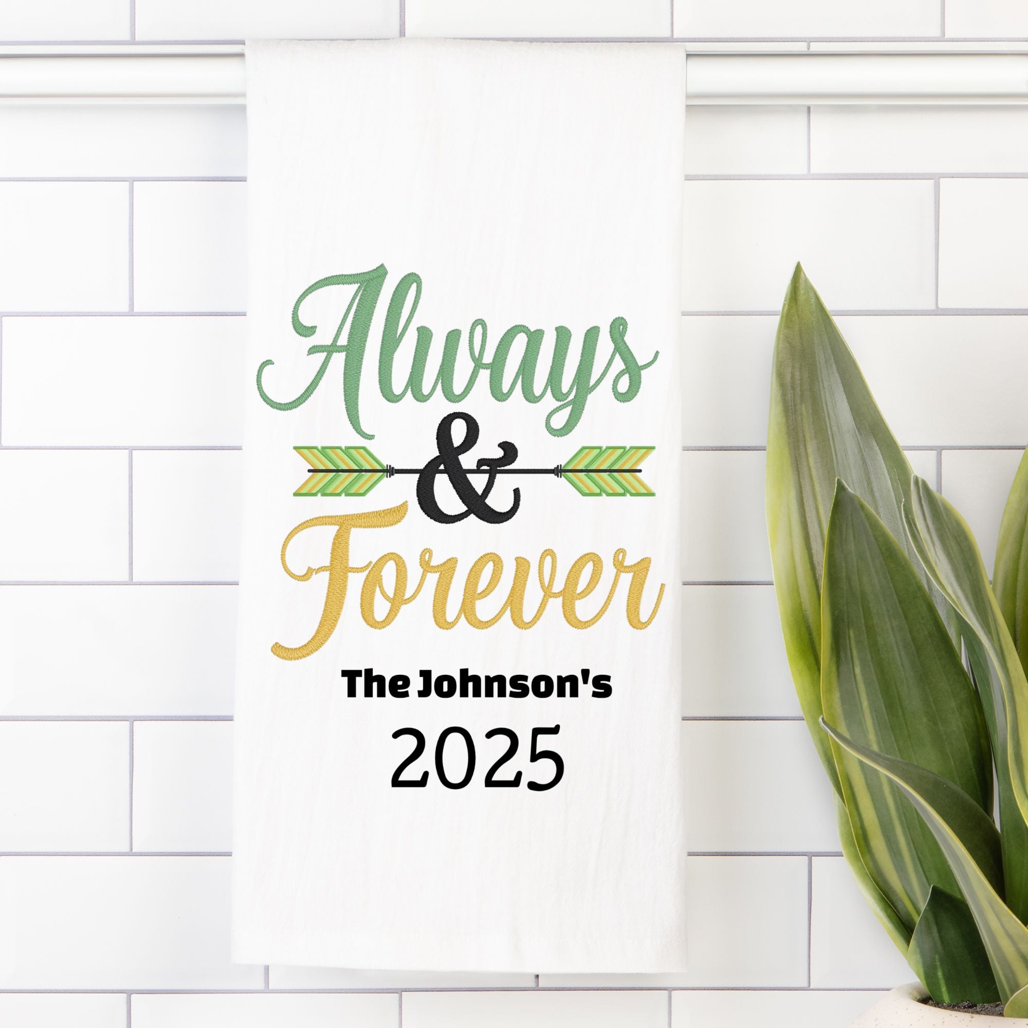 Decorative tea towel with 'Always & Forever' text on a white tiled wall with a plant.