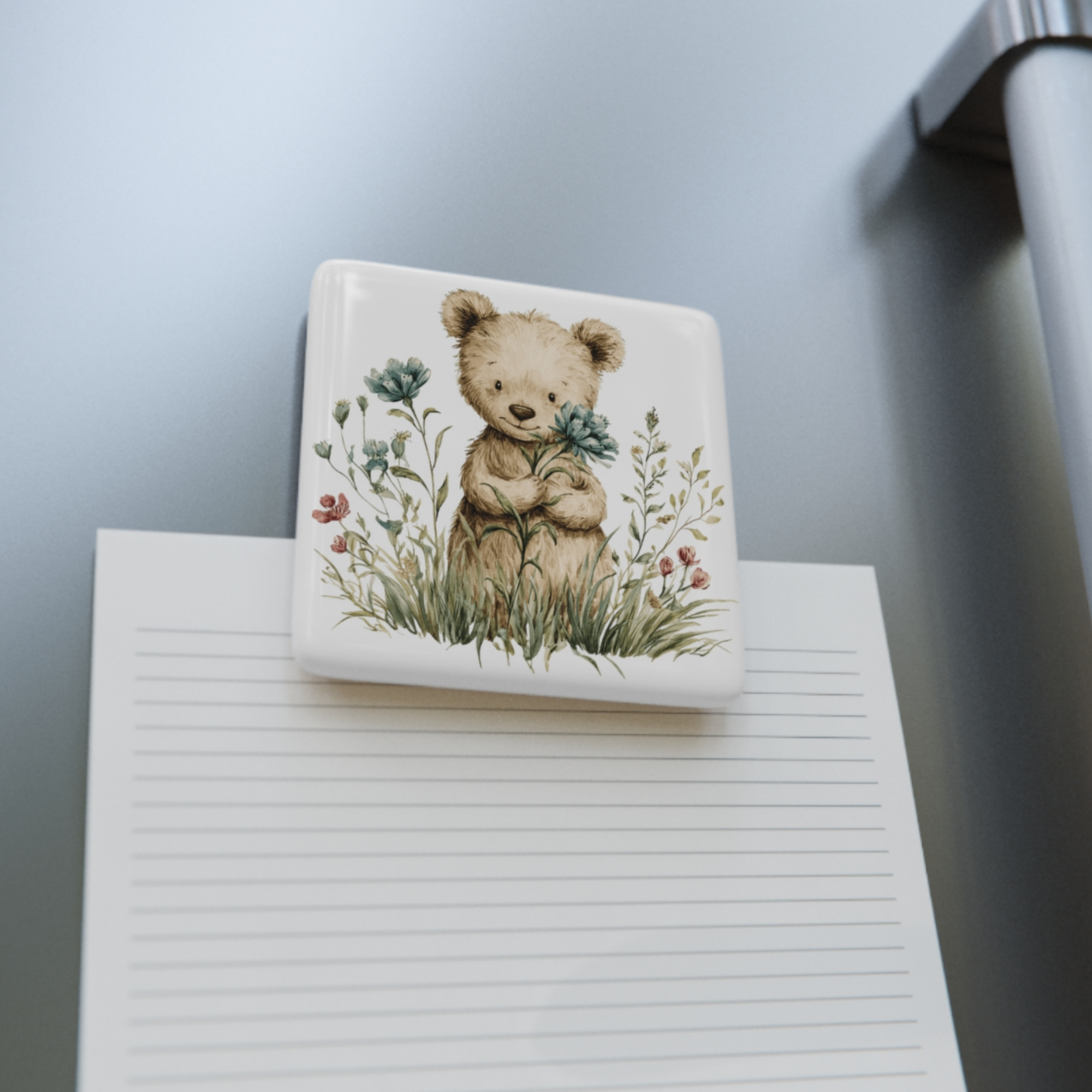 pad of paper with a square porcelain magnet with a teddy bear illustration on top of it