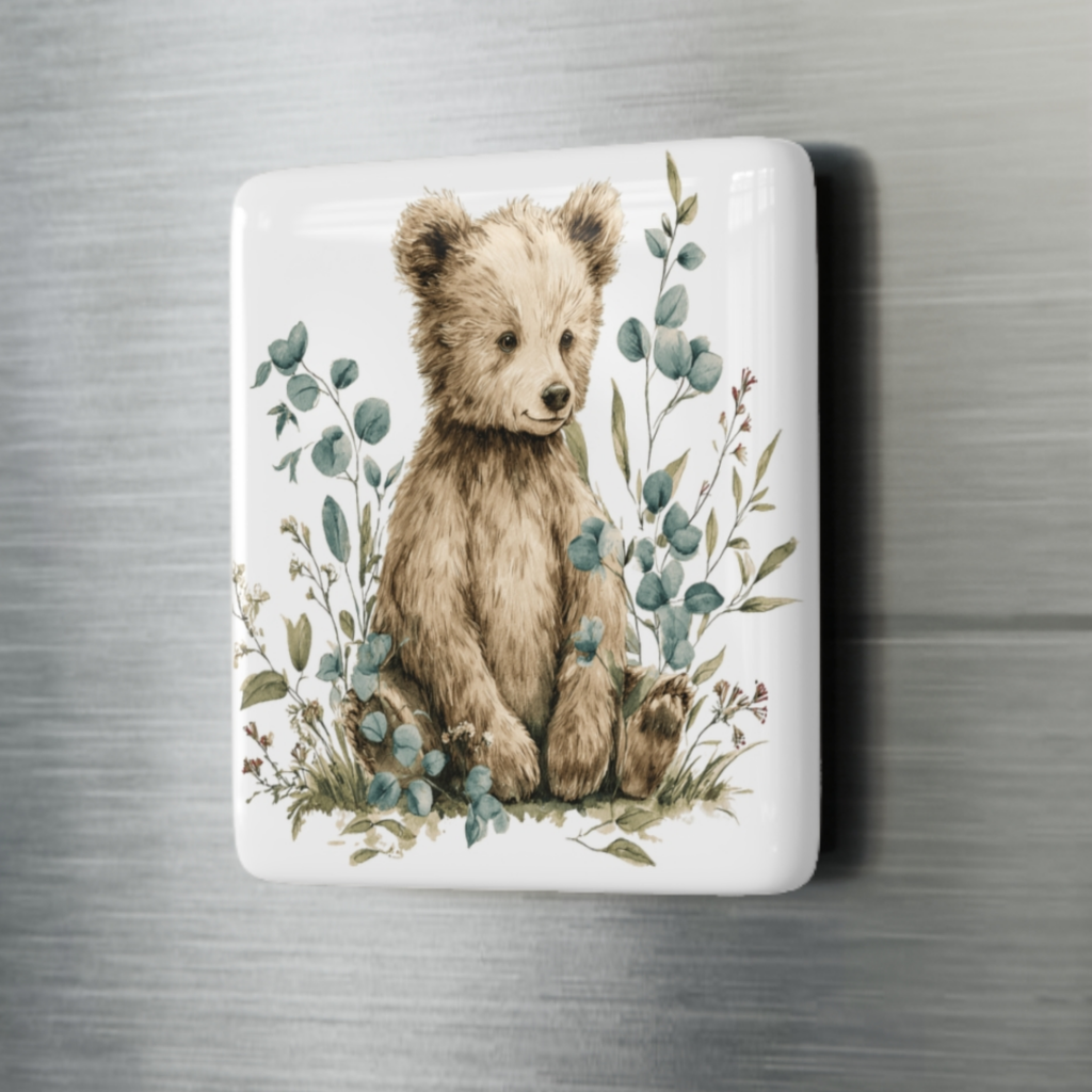 Fridge magnet with a bear illustration surrounded by leaves on a metallic surface
