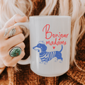Person holding a 15oz. mug with a dachshund illustration and 'Bonjour madame' text.