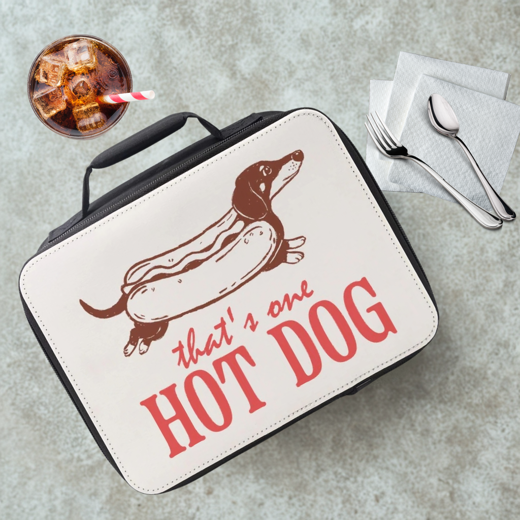 Lunch bag with a dachshund as a hot dog graphic and text 'that's one HOT DOG' on a cafeteria table with a drink and utensils.