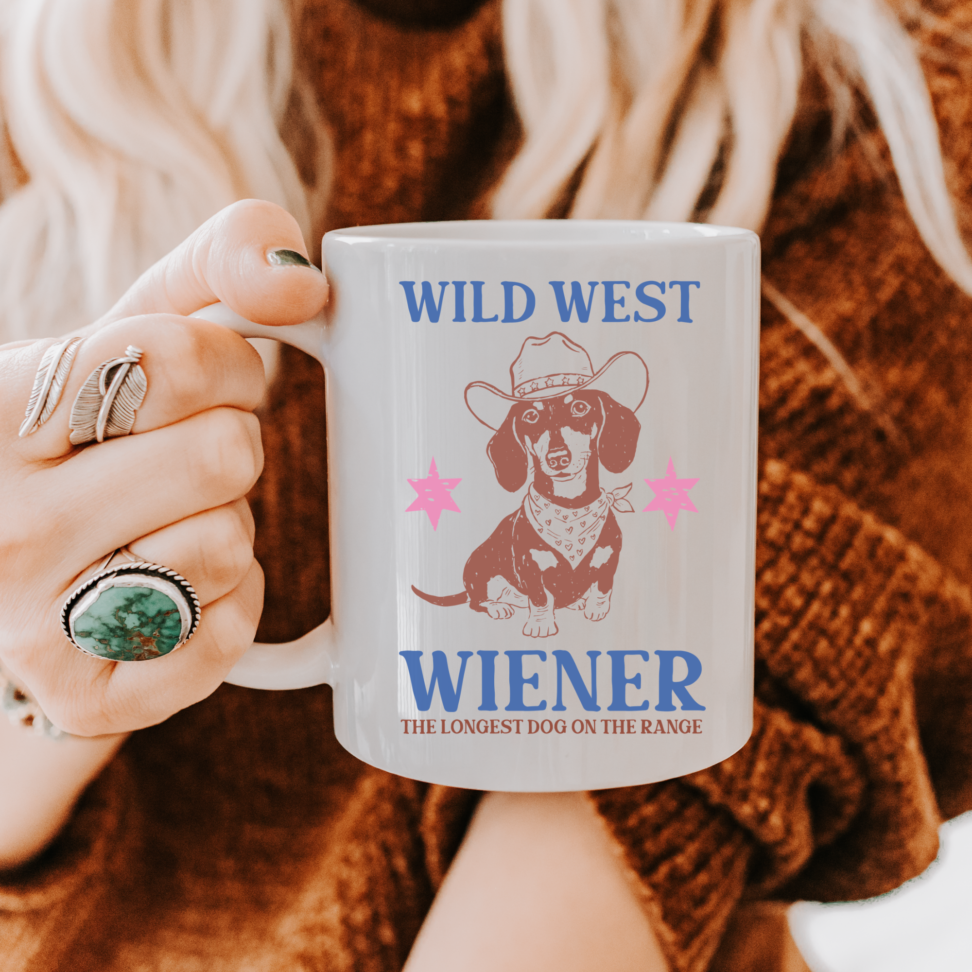 Person holding a 11oz mug with a dachshund graphic and text 'Wild West Wiener' against a textured brown background.