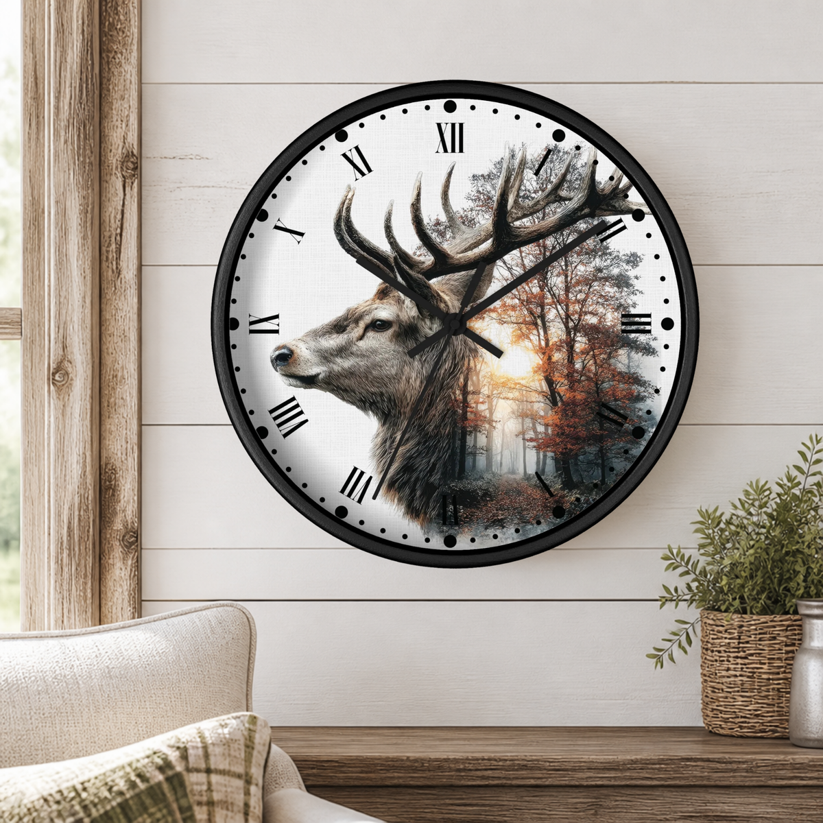 A round wall clock with a black frame hangs on a white shiplap wall above a wooden console table. The clock face features a detailed illustration of a stag deer head in profile against a forest scene with autumn trees and a glowing sun.