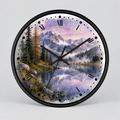 A round wall clock with a black frame and a scenic landscape print featuring mountains, pine trees, a lake, a herd of deer, and a purple sky. The clock face has black Roman numerals and black hands, photographed against a light gray background.