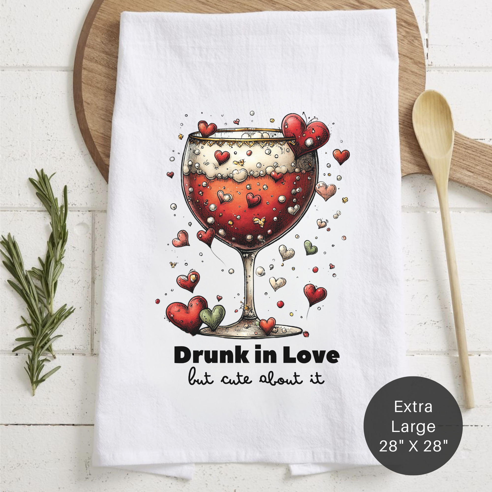 White towel with a wine glass design and text 'Drunk in Love but cute about it' on a wooden surface.
