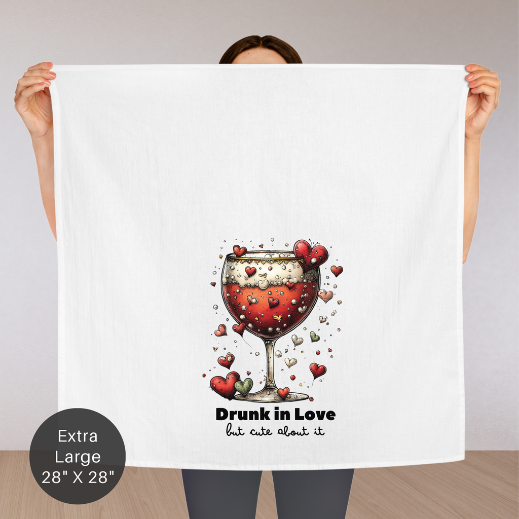 Person holding an extra large tea towel with a wine glass and hearts design, text 'Drunk in Love but cute about it', and size label 'Extra Large 28" x 28"'.