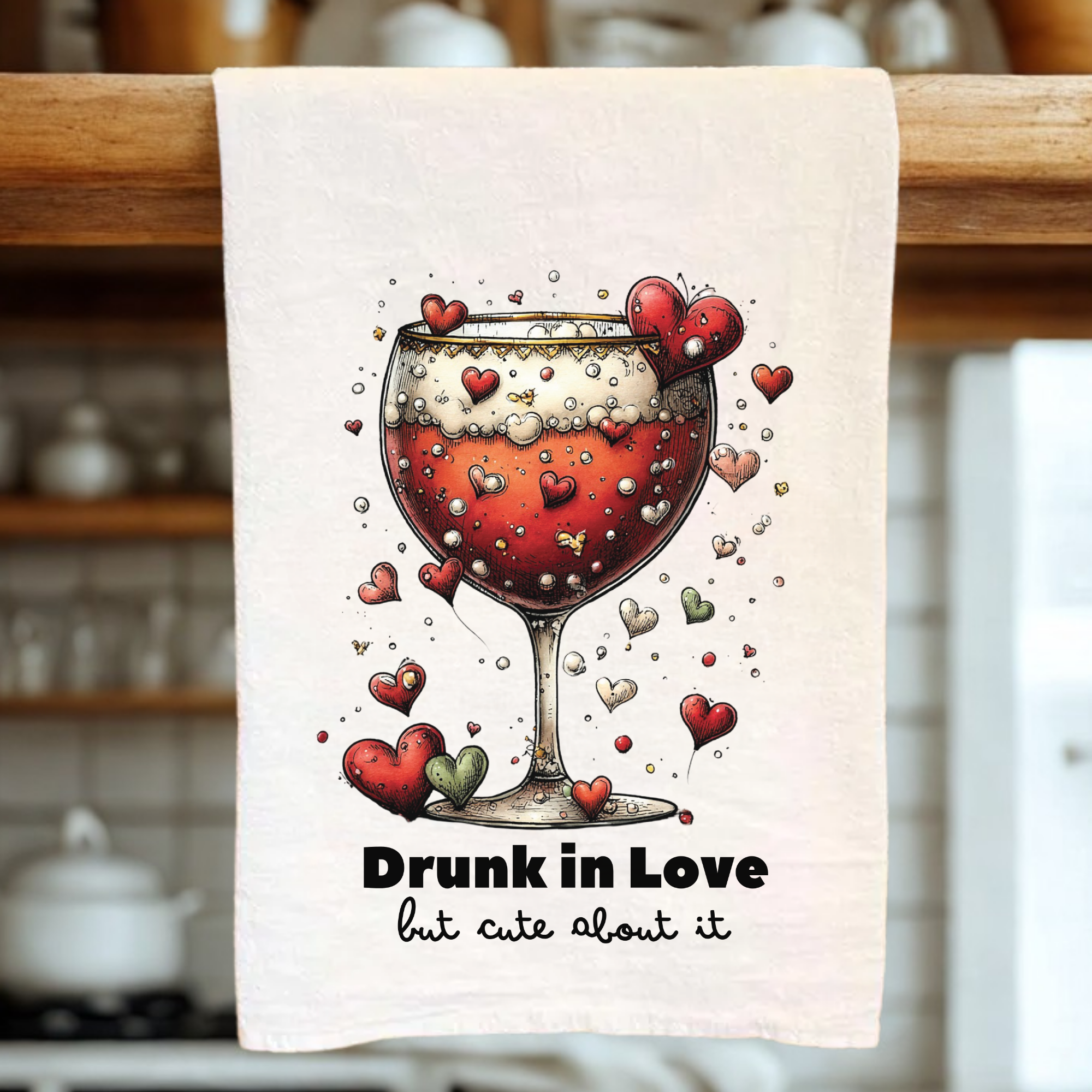 Kitchen towel with a wine glass and hearts design, text 'Drunk in Love but cute about it', hanging on a wooden rack.