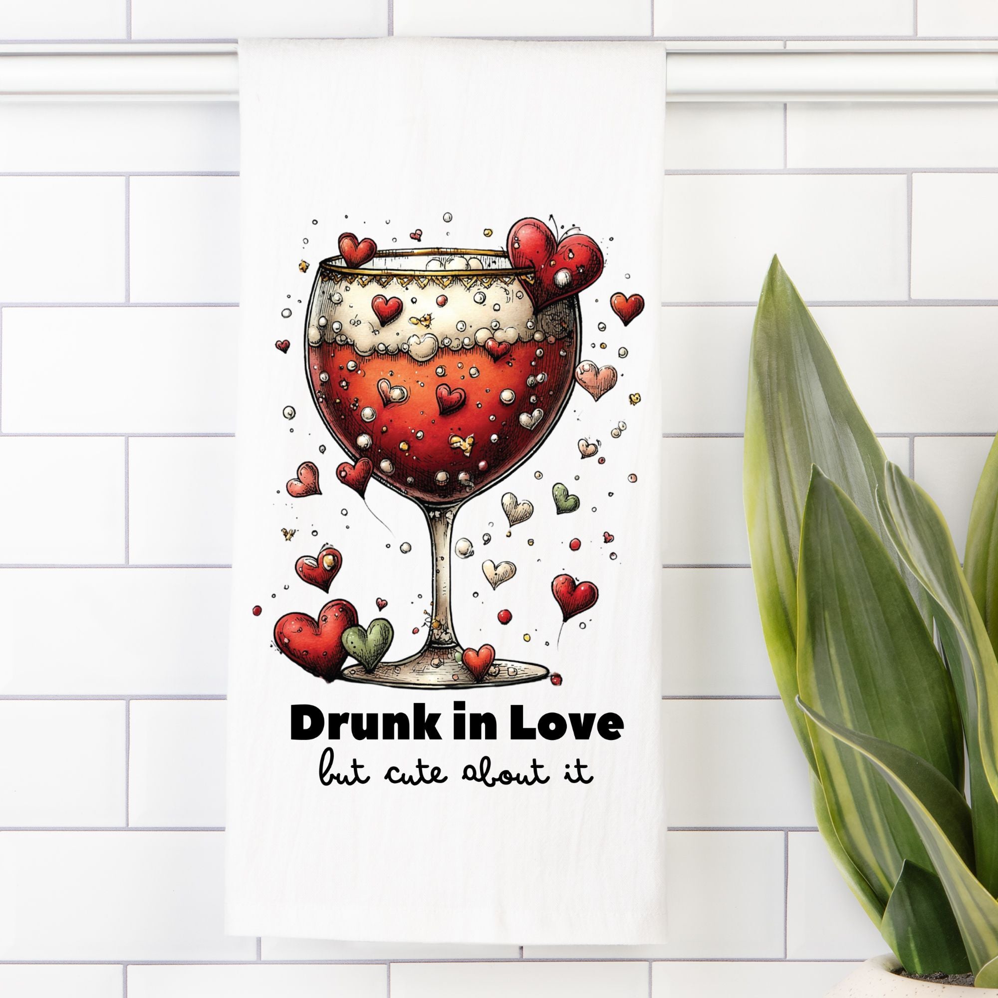 Tea Towle with Illustration of a wine glass with hearts and text 'Drunk in Love but cute about it' on a white tiled wall.