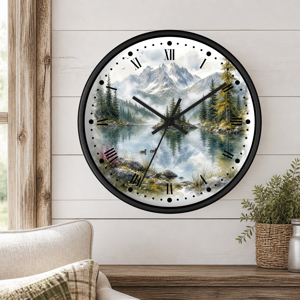 A round wall clock with a scenic mountain lake print, mounted on a white wood-paneled wall above a wooden shelf with a plant and part of a chair visible.
