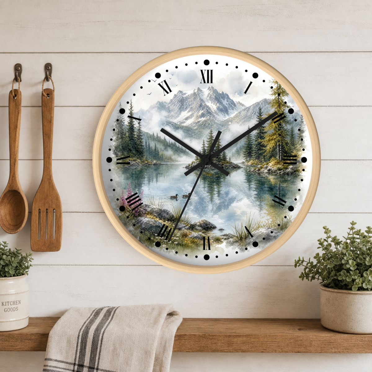 Round wall clock with a scenic mountain lake print, mounted on a white wood plank wall above a wooden shelf with kitchen utensils, plants, and a towel.