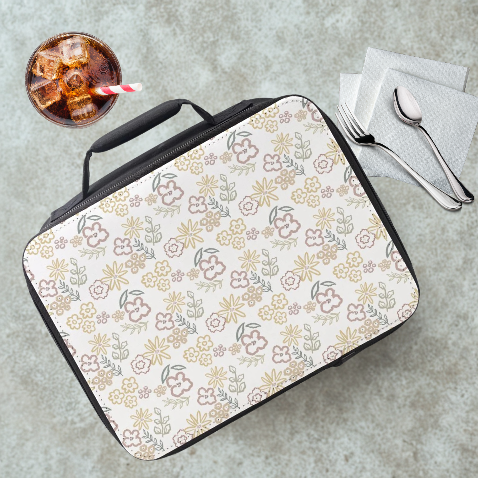 Floral-patterned lunch bag on a concrete surface with a drink and utensils.