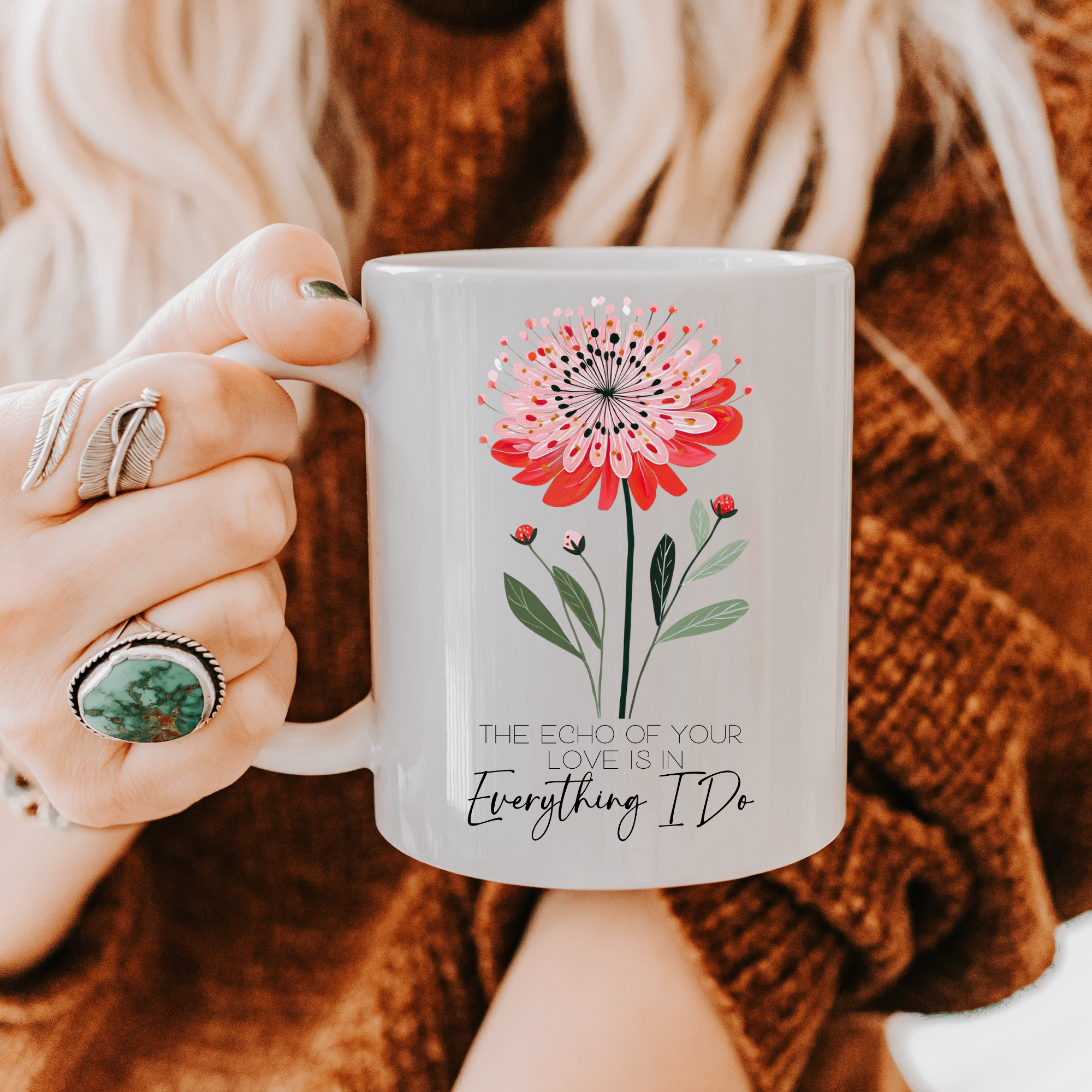 Person holding an 11oz mug with floral design and text 'The Echo Of Your Love Is In Everything I Do', wearing a brown sweater.